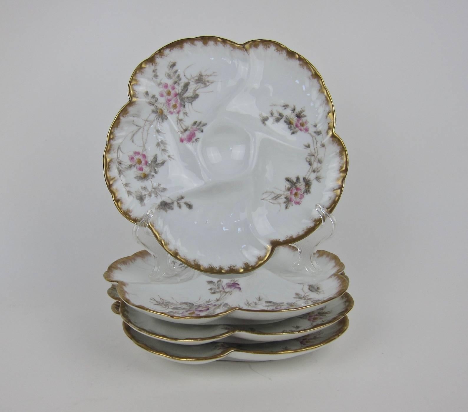 A set of four antique French porcelain oyster plates from Société Gérard, Dufraisseix and Morel (formerly Charles Field Haviland) of Limoges, France. The molded 'Wave' pattern plates have five wells for oysters over ice surrounding a smaller,