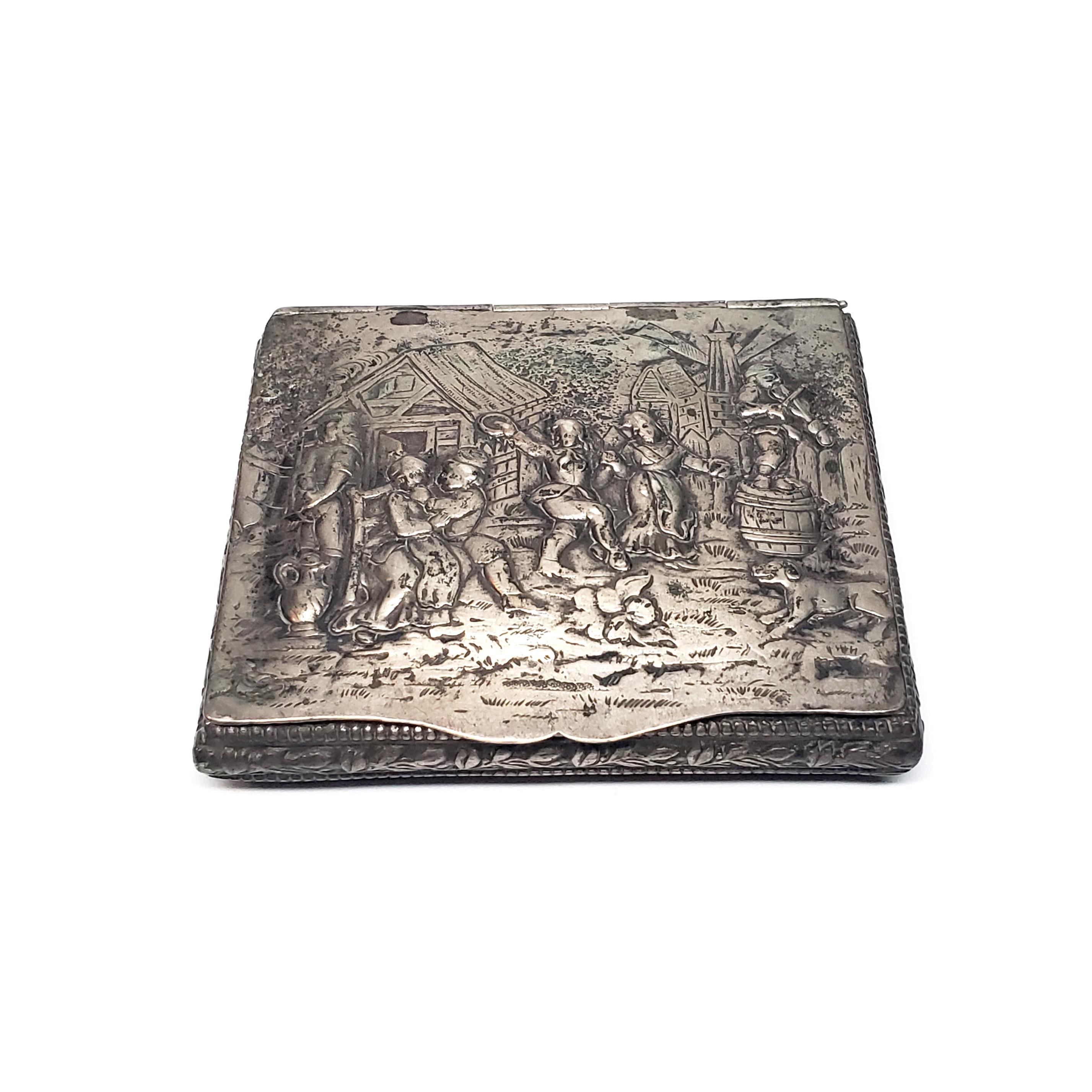 Antique German 800 silver hinged cigarette box.

This is a beautiful example of German Hanau silver, this box could have been used for cigarettes, or cards. The lid depicts a village scene of dancing and music making. Leaf and beaded design all