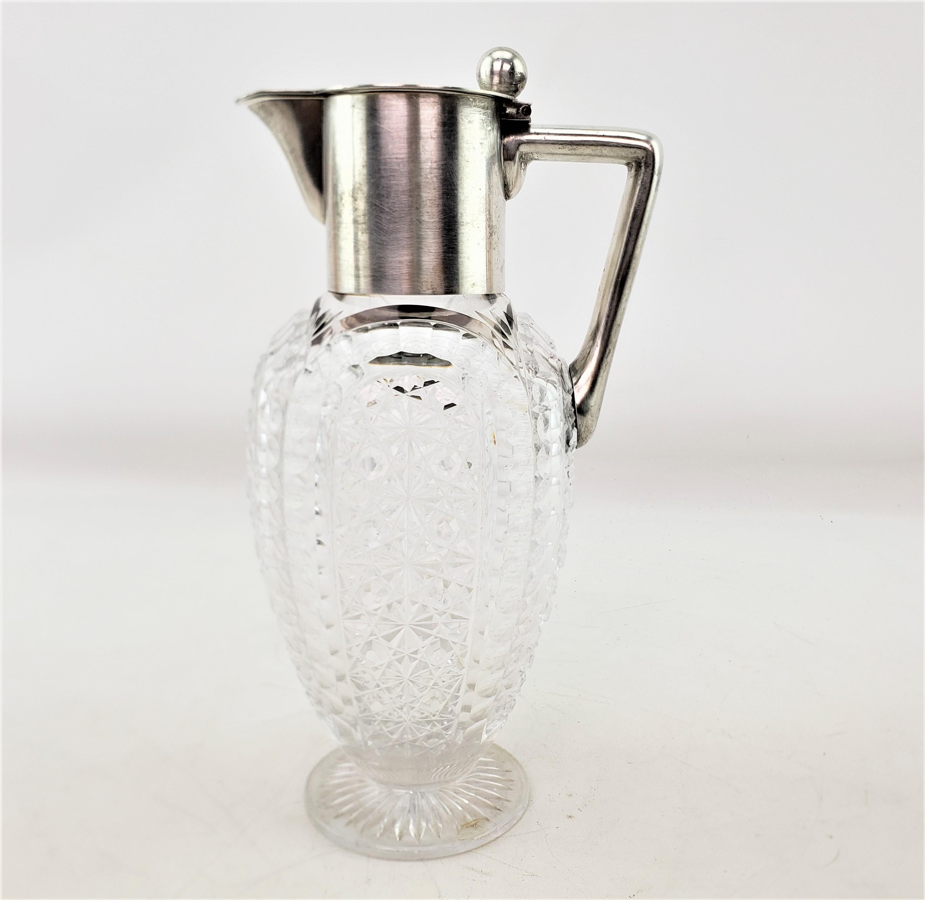 This antique claret jug is hallmarked by an unknown maker, and believed to have originated from Germany and date to approximately 1920 and done in the period Art Deco style. The body of the jug is composed of a very heavy and deeply cut crystal with
