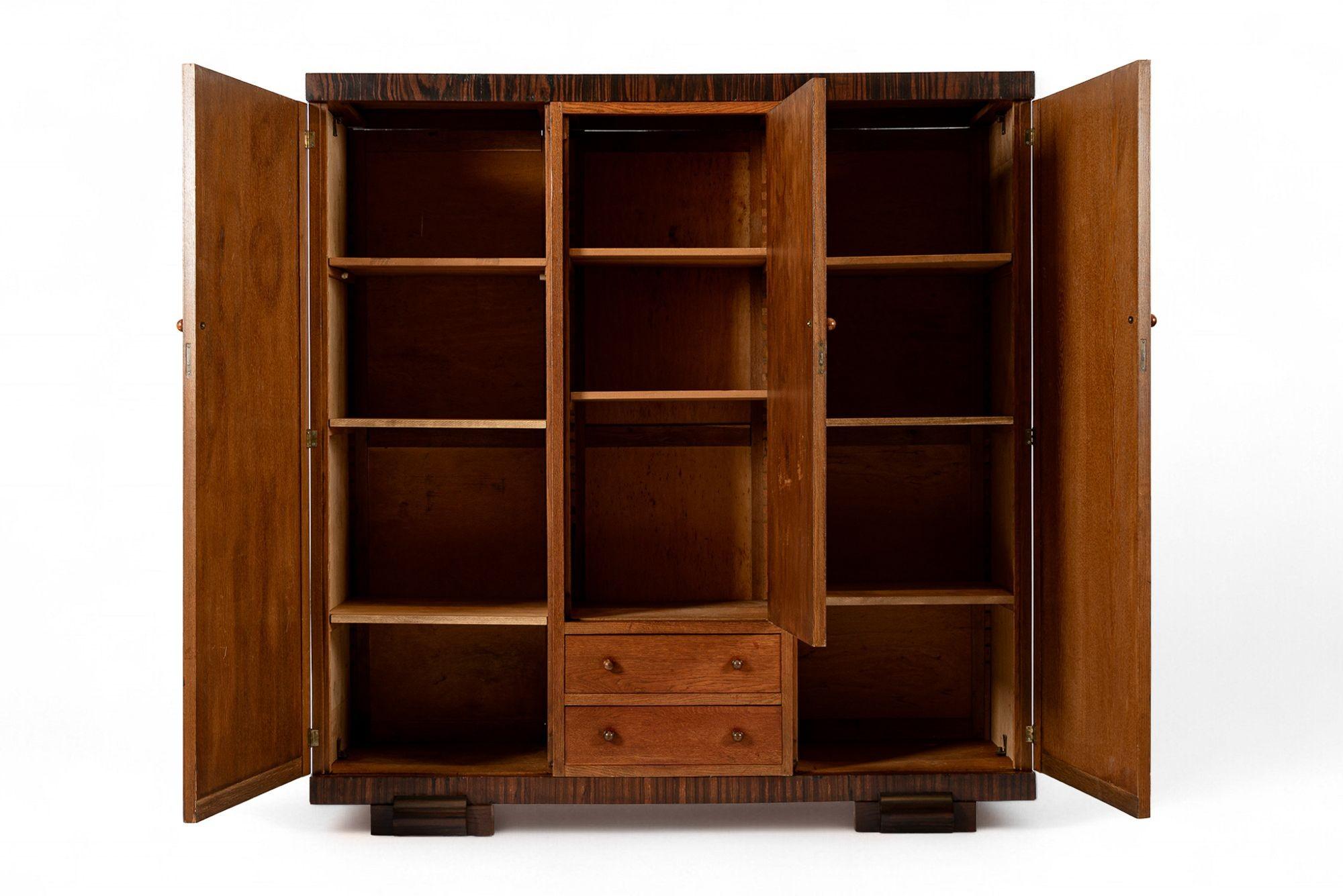 Cette étonnante armoire à linge en bois de l'Arte Antiques CIRCA date d'environ 1930. L'élégant design géométrique en bois bicolore est impeccablement fabriqué à la main en bois de hêtre massif avec des accents d'incrustation en ébène de Macassar.