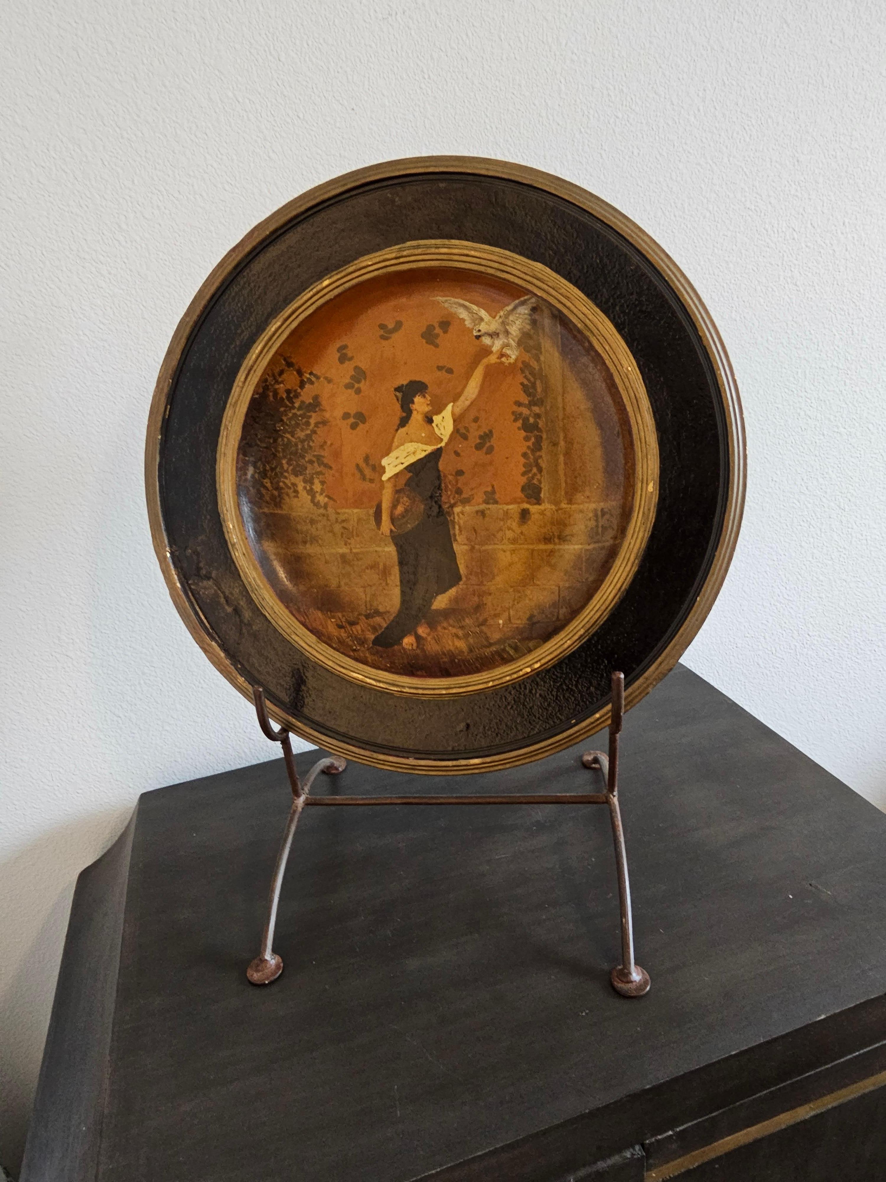 A beautiful hand-crafted and hand-painted terra-cotta charger wall plaque, Germany, early 20th century, featuring an exceptional painted scene with woman and bird in courtyard, signed with maker's mark at circular foot back (illegible), intact with