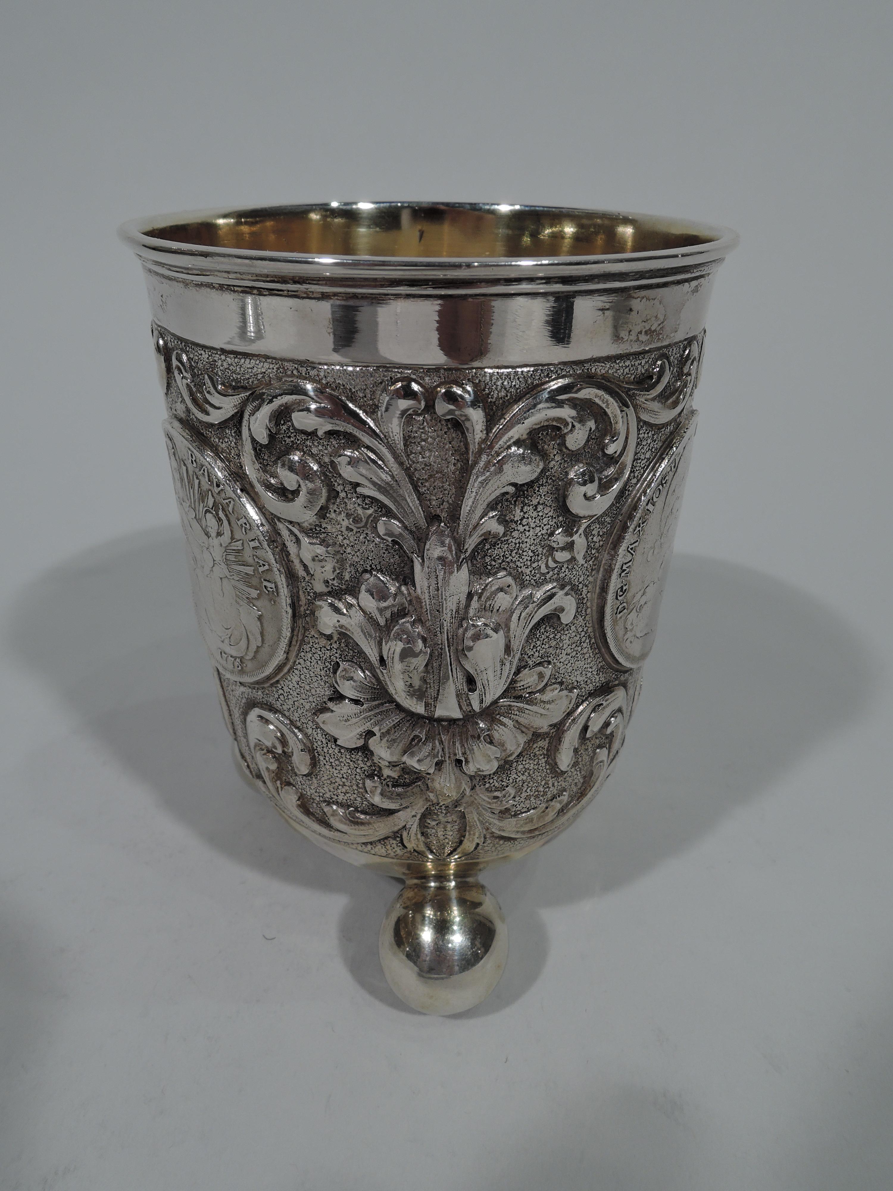 Gobelet en argent 830 de style baroque allemand, vers 1900. Des côtés droits et un fond incurvé montés sur 3 boules hors gabarit. Des fleurs et des volutes fluides encadrent des pièces insérées avec des armoiries et des bustes classiques entourés de