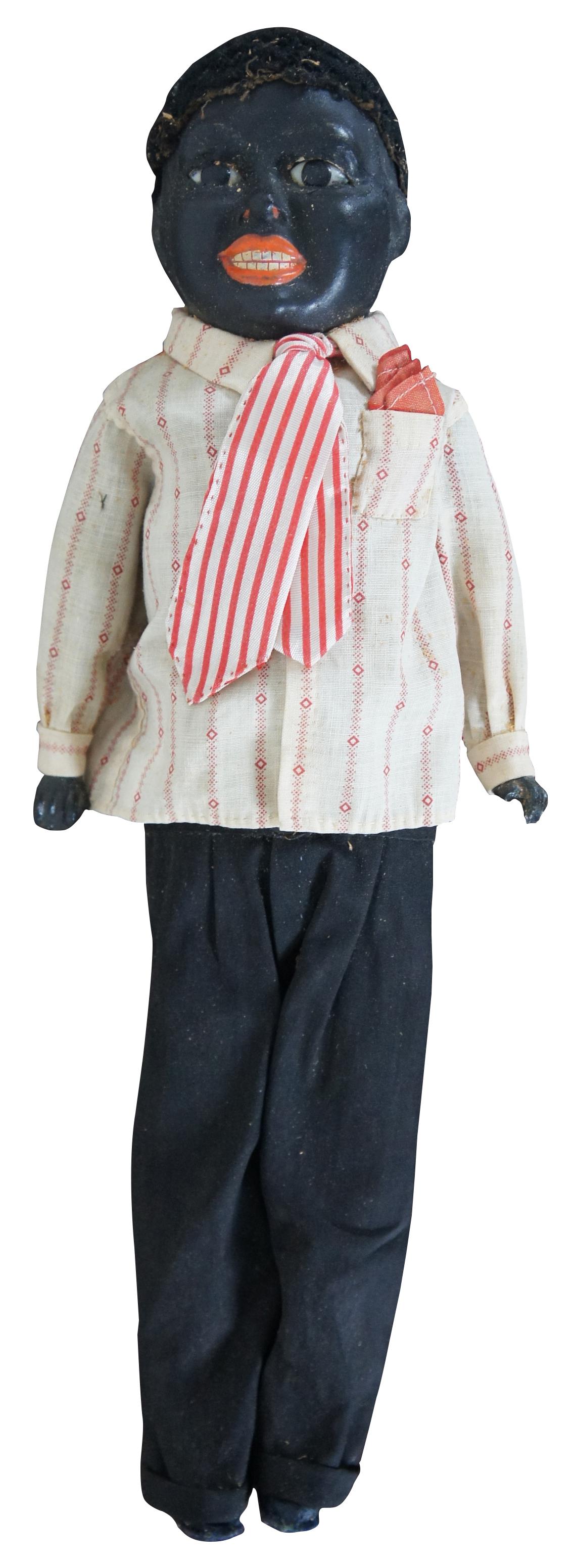Antique 19th century black doll shaped like a young boy with bisque head, hands and feet, glass eyes, and sawdust filled cloth body, dressed in a striped shirt, matching tie and pocket square, black pants and navy blue leather shoes. Measures: