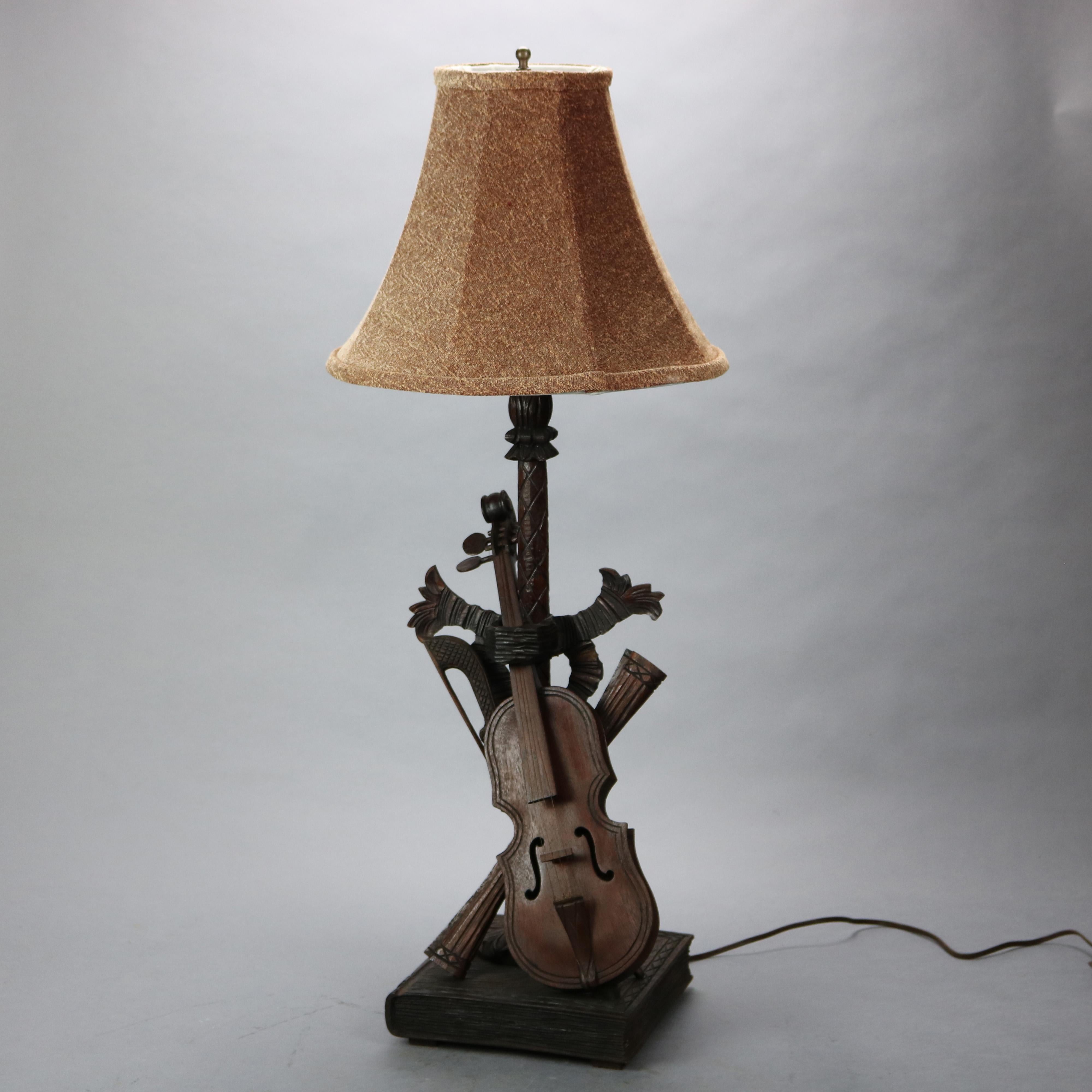 Antique German Black Forest table lamp offers carved sculptural base with music instrument grouping to include violin, bow and book, wired for US electrical use, c1880

Measures - overall 34.25''h x 14''w x 14''d; shade 14'' diameter; base 9'' x