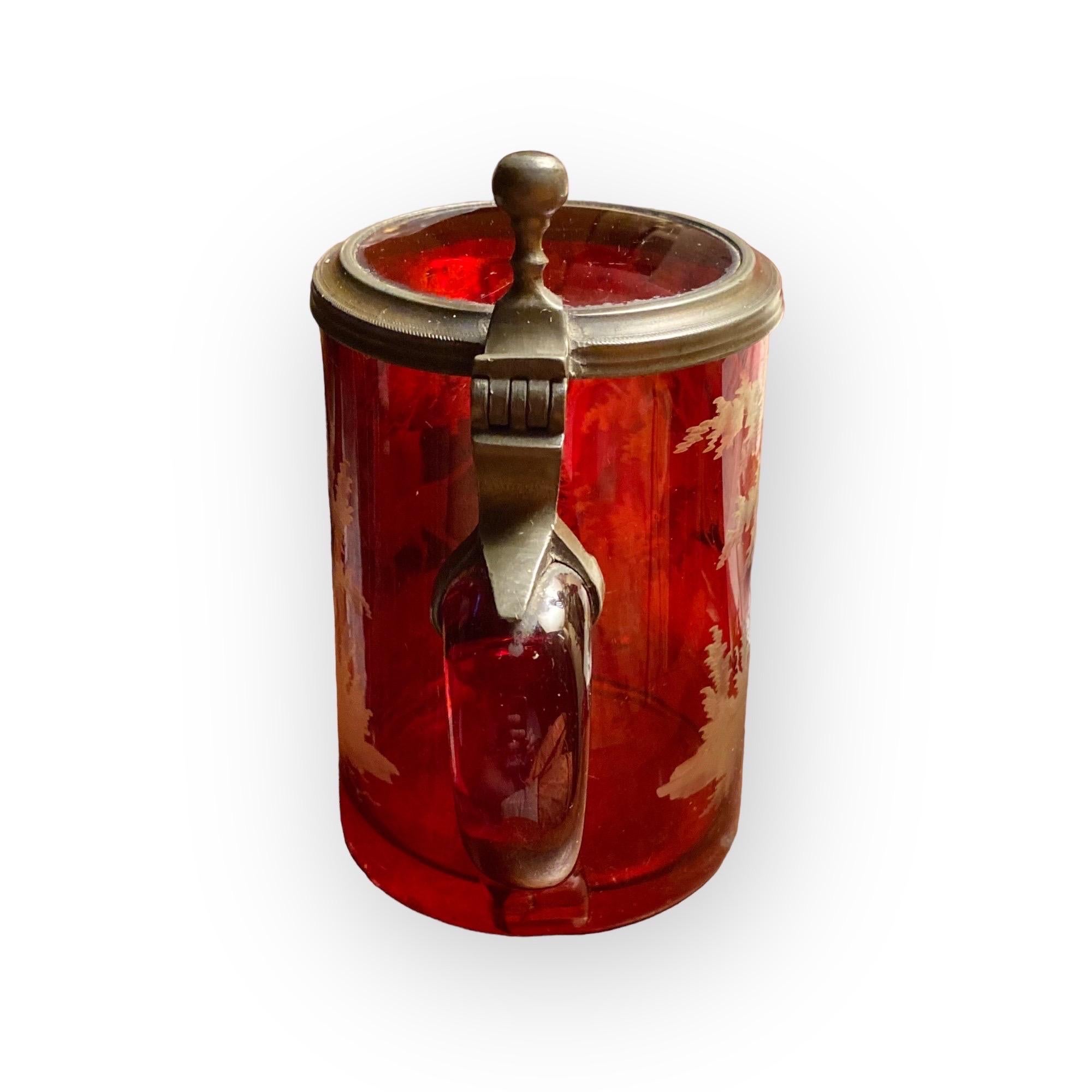 A stunning antique Bohemian etched red flash glass beer stein. It dates to the mid-19th century. This item has been handcrafted utilizing glass
etching and engraving depicting a wooded scene and a hunting dog. Its primary trait is the rare intense