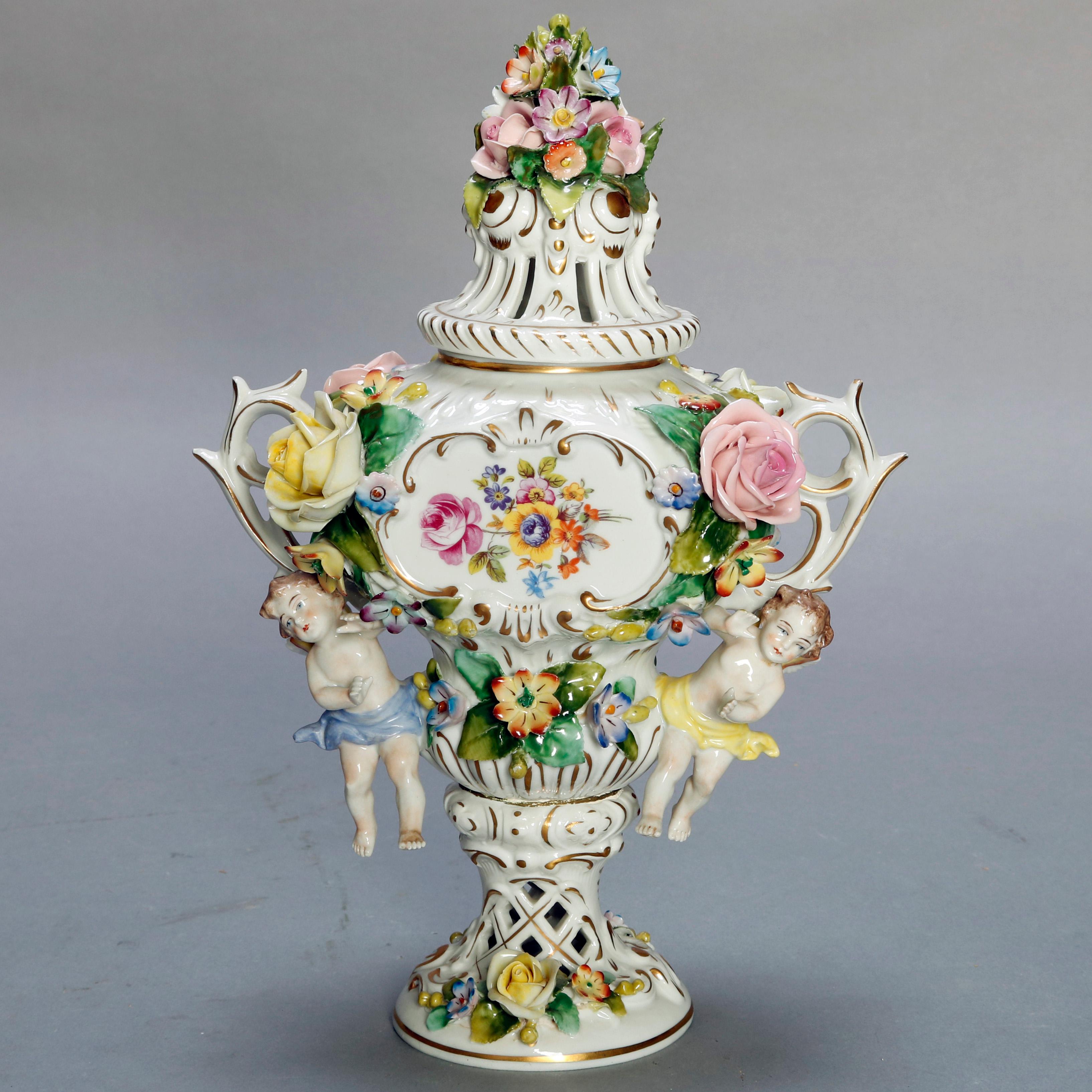 An antique pair of classical German Dresden Sitzendorf porcelain urns each offer central hand painted floral reserves, pierced floral lids, double stick form handles with cherubs, overall applied flowers, raised on pierced plinth with garden