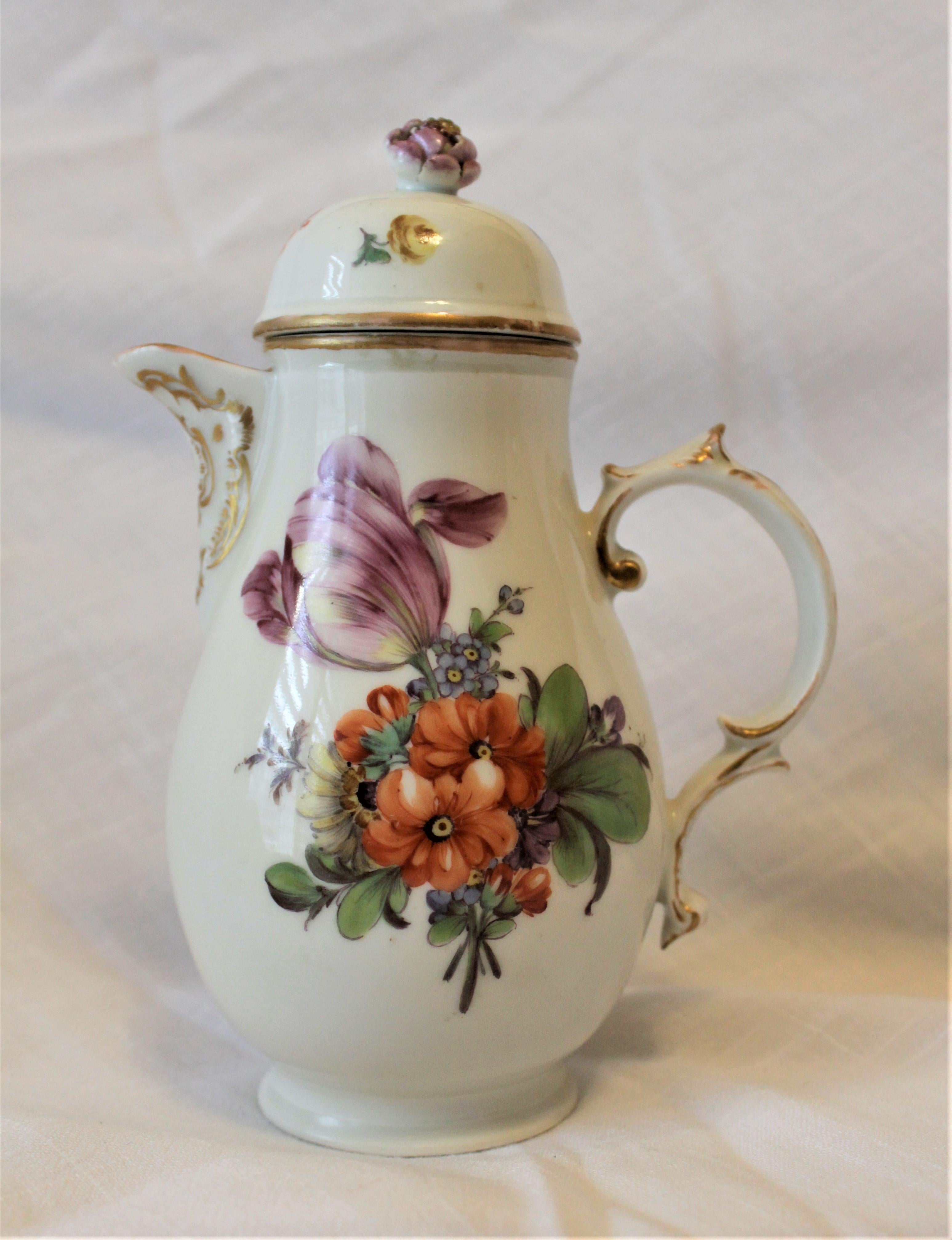 This antique German porcelain coffee pot was made by the Furstenberg Works factory in circa 1760 in the period Rococo style. This coffee pot is decorated with hand painted flowers in vibrant colors on the sides which is accented with fire gilt