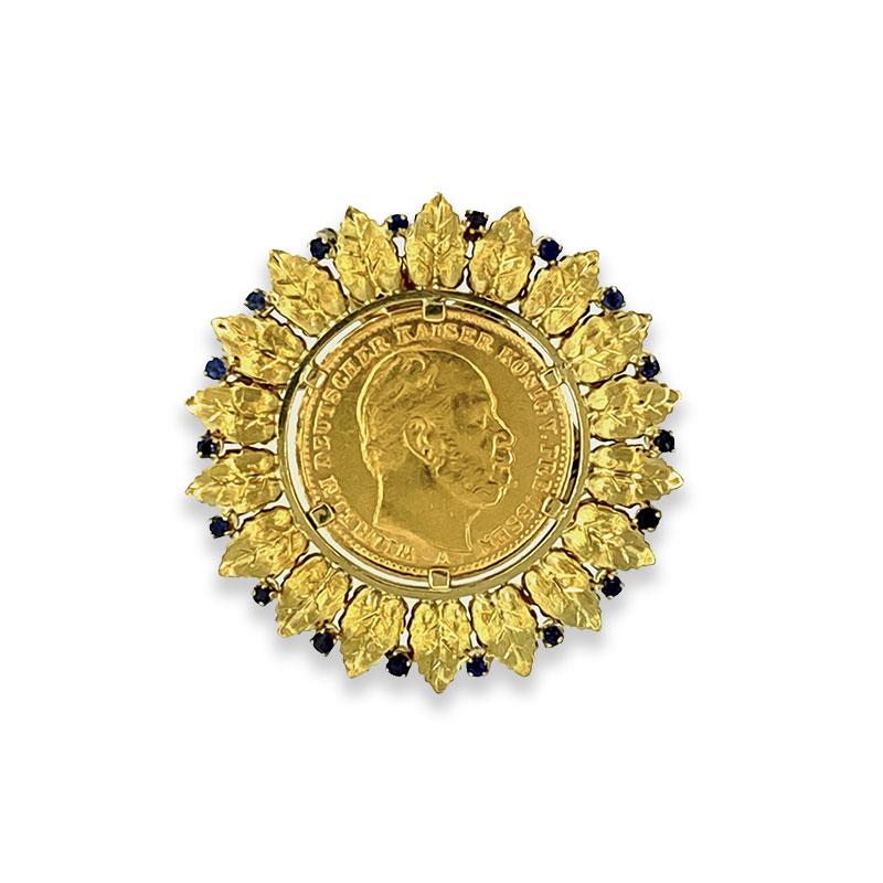 A 1887 20 Mark gold coin haloed by a 22K yellow gold leaf design with 0.23 carats of round cut blue sapphires. This brooch cleverly doubles as a pendant with its hidden loop on the back side.  

Brooch Length: 1.55 inches

Brooch Width: 1.55 inches