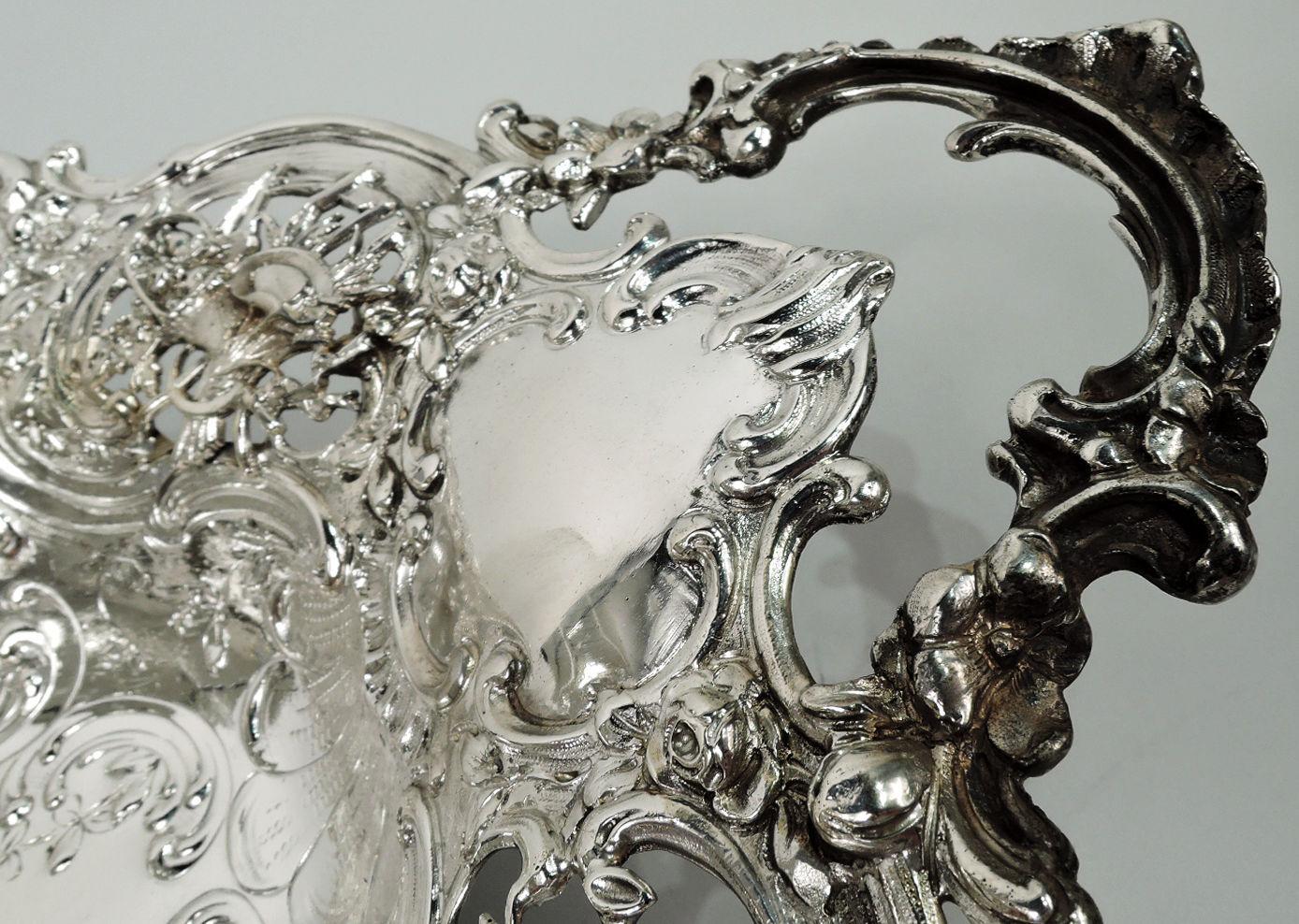 German Rococo 800 silver bowl, ca 1910. Oval with scroll and shell rim and leafing scroll and flower end handles. Well has chased scene of cherub frolics. Same on shoulder alternating with trophies in openwork. Chubby-thighed, adroitly-draped