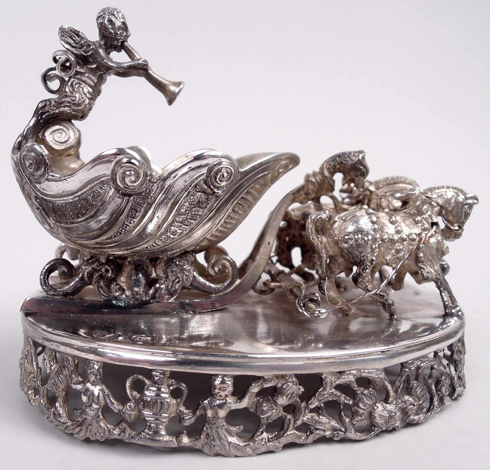 Sale aperto rococò tedesco in argento, 1900 circa. Un cherubino alato è inginocchiato sul retro di una slitta trainata da cavalli rampanti su rotaie. Montato su una base ovale; i lati sono aperti con un vaso e un bordo di ninfe. Marchi di Hanau.