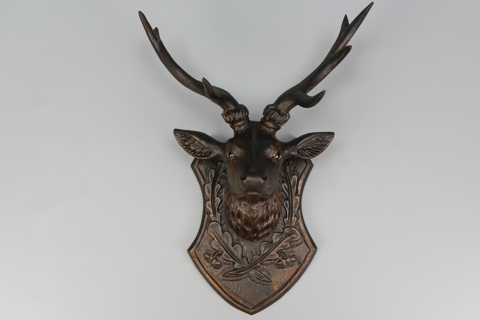 Antique Black Forest-style German hand-carved linden wood deer head on a carved wall plaque.
An impressive antique hand-carved wall-hanging deer head made of linden wood with wooden antlers and glass eyes, mounted on a carved ornate wooden plaque