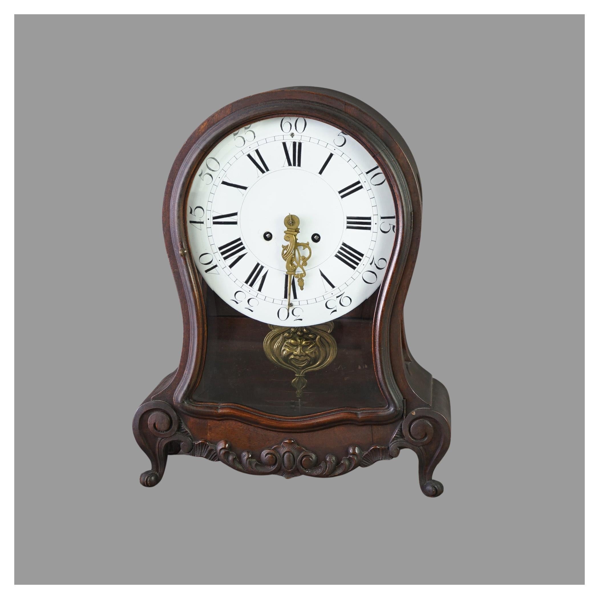 An antique German mantle clock offers mahogany case in hourglass form with foliate carved decoration, having glass door opening to interior with porcelain face, and raised on scroll form feet; marked Germany as photographed; c1880

Measures - 18.5