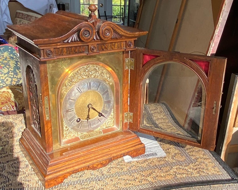 This Antique Lenzkirch German mantel clock made of walnut burled wood case has a scroll finial to the top with urn pediments. Te brass PLACK is inscribed 