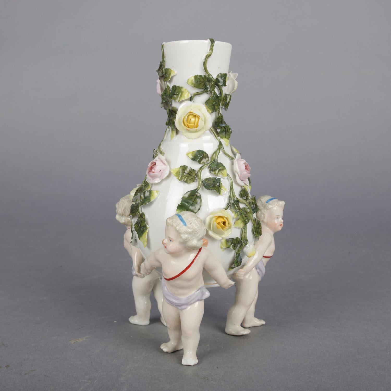 An antique figural German Meissen Porcelain bud vase features vessel with bulbous form and flared neck having all over applied and hand painted floral roses with leaf and vine, raised on three cherub form legs, crossed sword mark on base, circa
