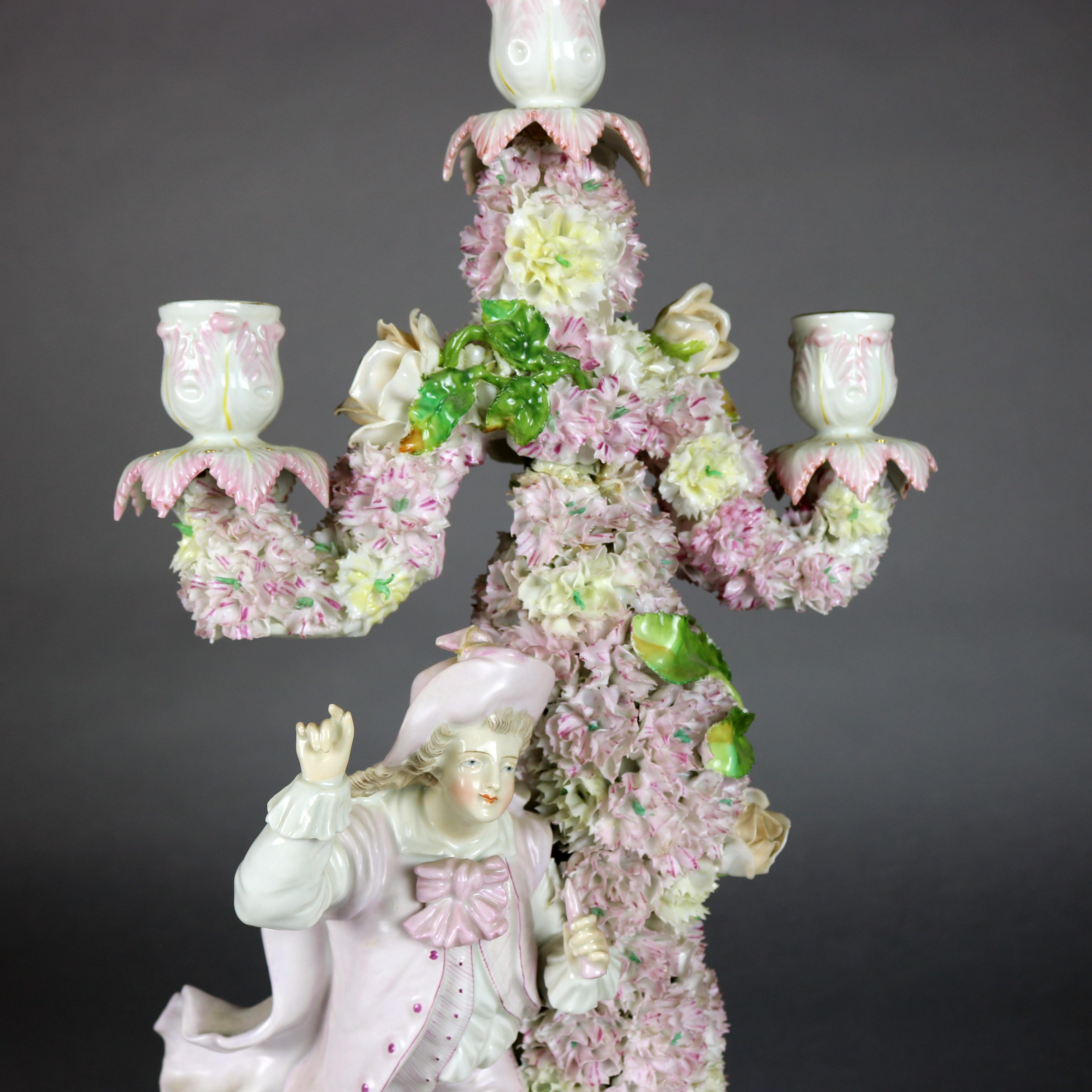 A figural German Meisen School garniture set includes pair of three light candelabra and central footed bowl in hand painted porcelain with all-over applied floral and foliate decoration, the candelabra each with male and female courting couple