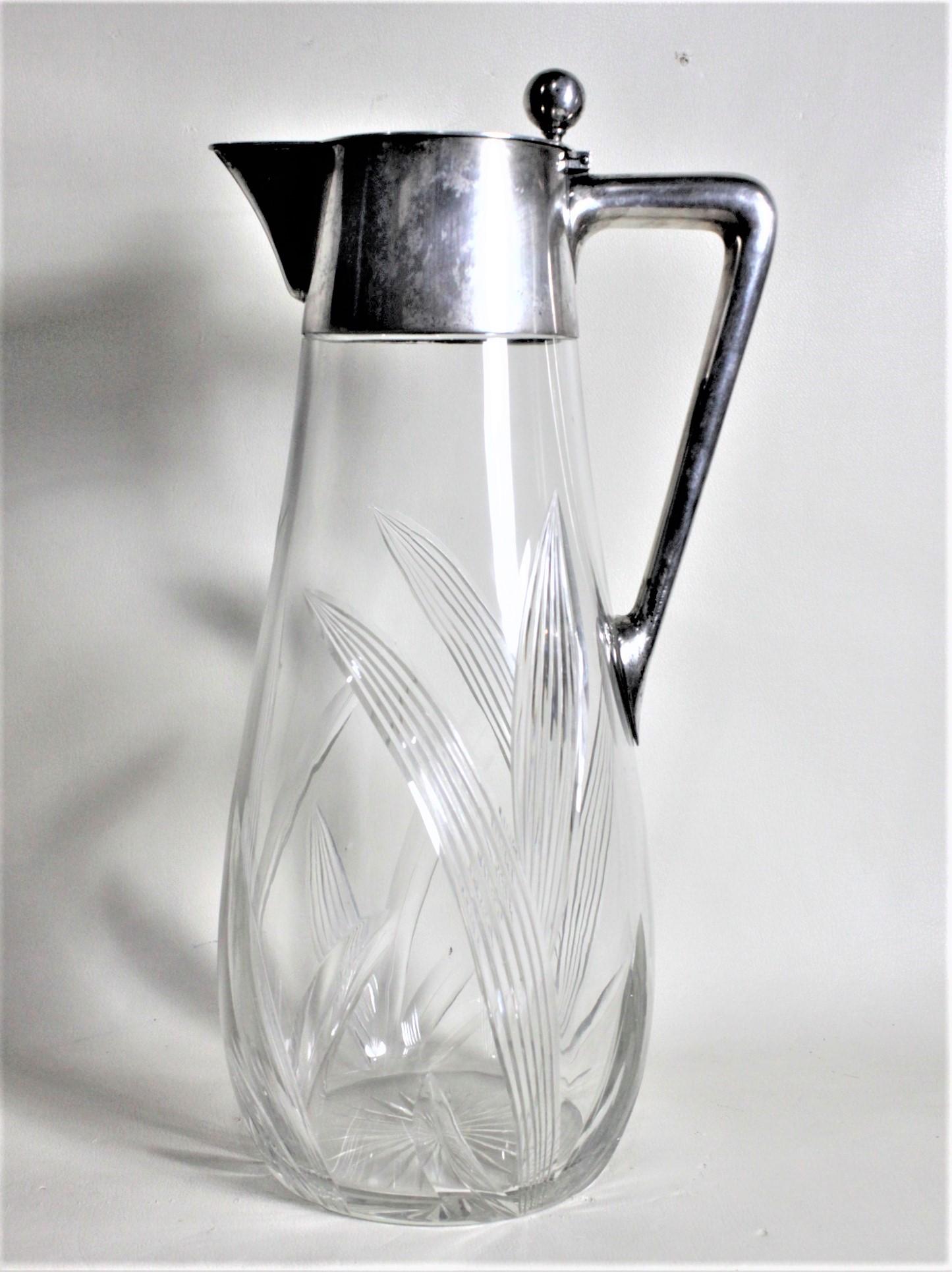 This antique German cut crystal and .800 silver lidded pitcher was made by a Julius Merz in circa 1900 in the period Edwardian style. The collar and handle of the pitcher are made of silver and the lid has a very detailed ball top to open the lid.