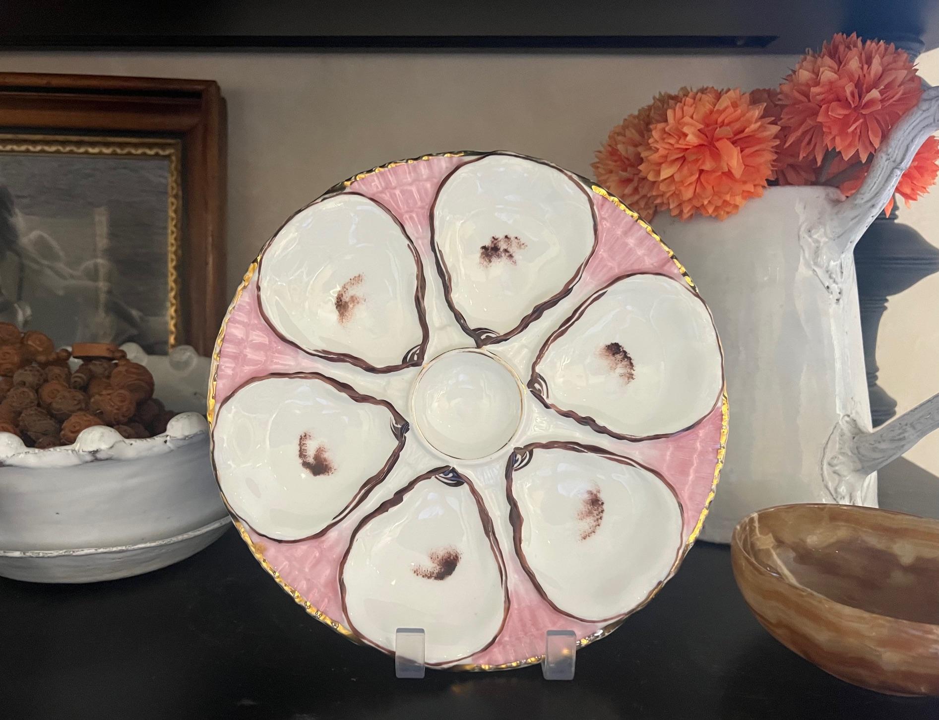 Antique oyster plate made by Carl Tielsch in the late 19th century in Germany.  The plate has six wells for oysters and a center well for lemon wedges. The background is a vivid pink with a gold rim. Hallmarked on the bottom for Carl Tielsch.