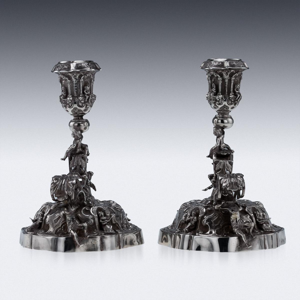 Antique early 20th century German pair of exceptionally decorative solid silver figural chambersticks, each of shaped-circular form, profusely chased with scrolls, four arches set with figures in 17th century clothes playing and singing, the