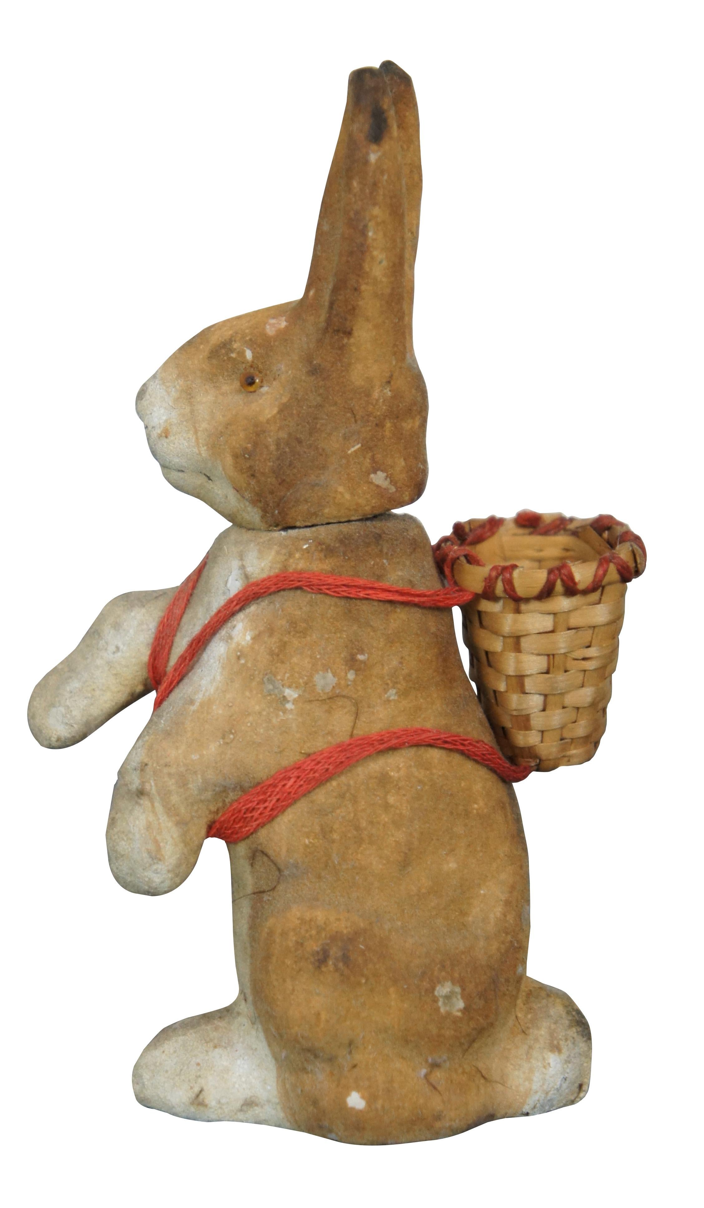 Early 20th century German paper mache Easter candy container in the shape of a brown rabbit seated upright, with brown glass eyes and wearing a basket on its back. Head acts as stopper.