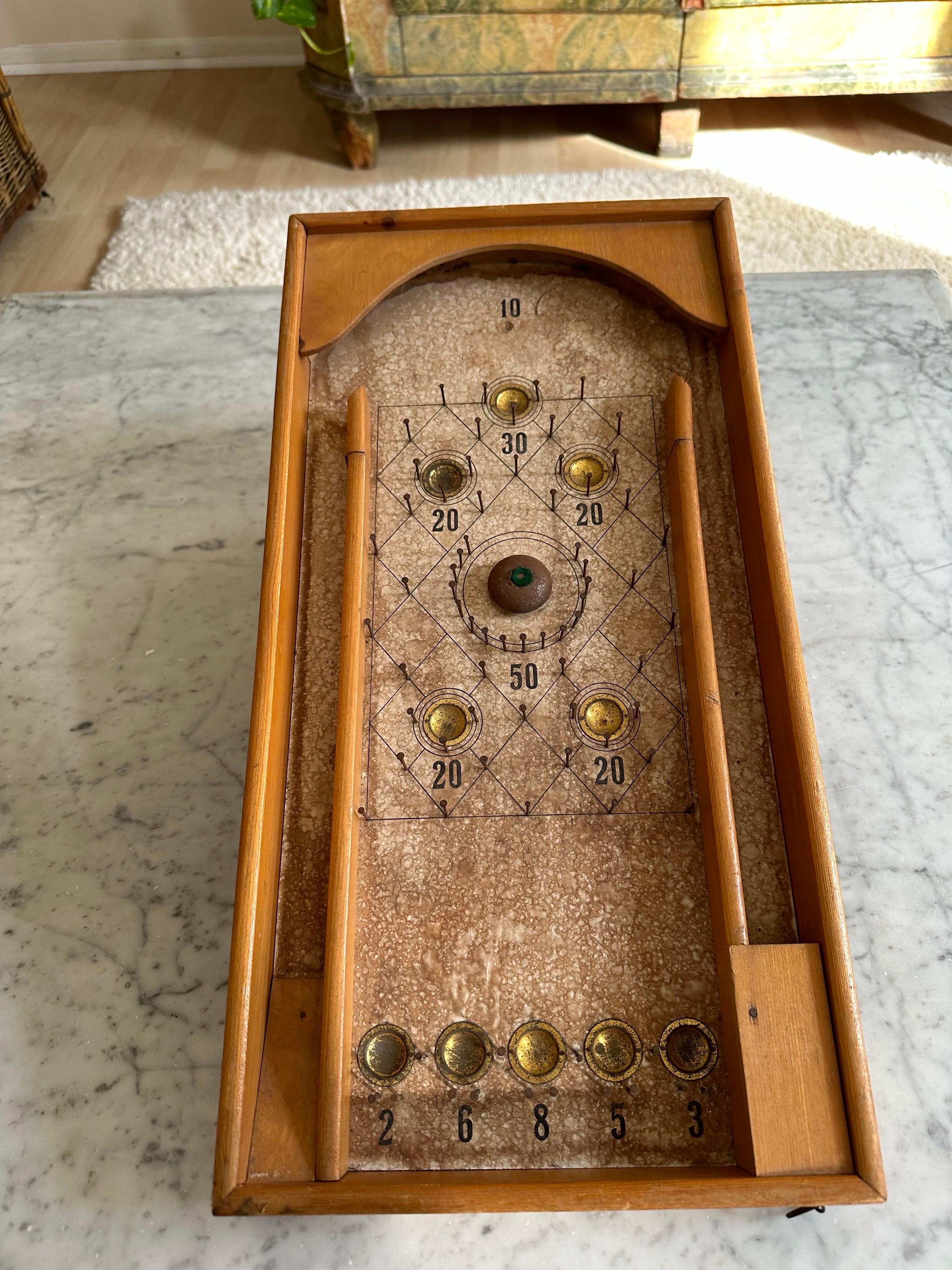 Questo antico flipper in legno, realizzato in Germania intorno al 1920, è un raro e affascinante esempio di artigianato dei primi del Novecento. Il suo corpo è costruito in legno massiccio, mentre il display è caratterizzato da carta vintage che