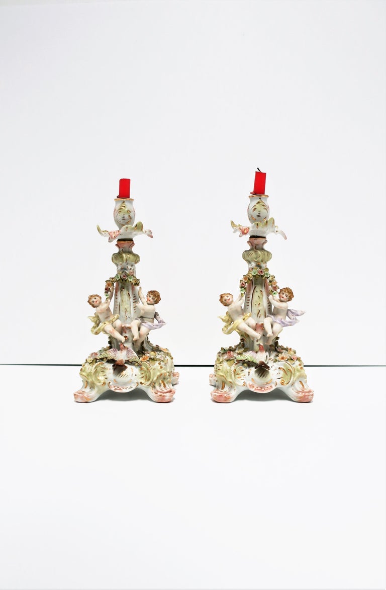 A beautiful pair of antique German white porcelain candlestick holders, in the Rococo style, circa late 19th century, 1880s, Germany. Beautiful details: light pastel colors, gold gilt, small flowers and leaves, putti/cherubs and bird/dove at bottom