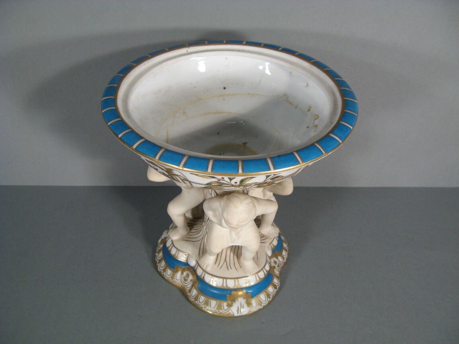 This exquisite antique coupe features colorful floral and botanical decorations in polychrome porcelain. Supported by three Atlas figures in porcelain biscuit, this piece showcases a grand design reminiscent of the late 19th to early 20th