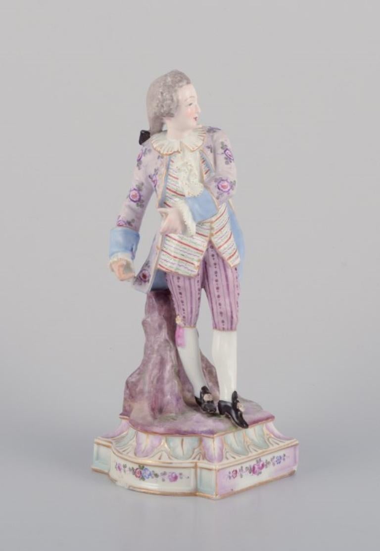 Antique German porcelain figurine of a young man in fine clothes. 
Hand-painted in polychrome colors.
19th century.
Marked.
In good condition with visible signs of restoration on the left hand, missing thumb, and some chips on the base. Please refer