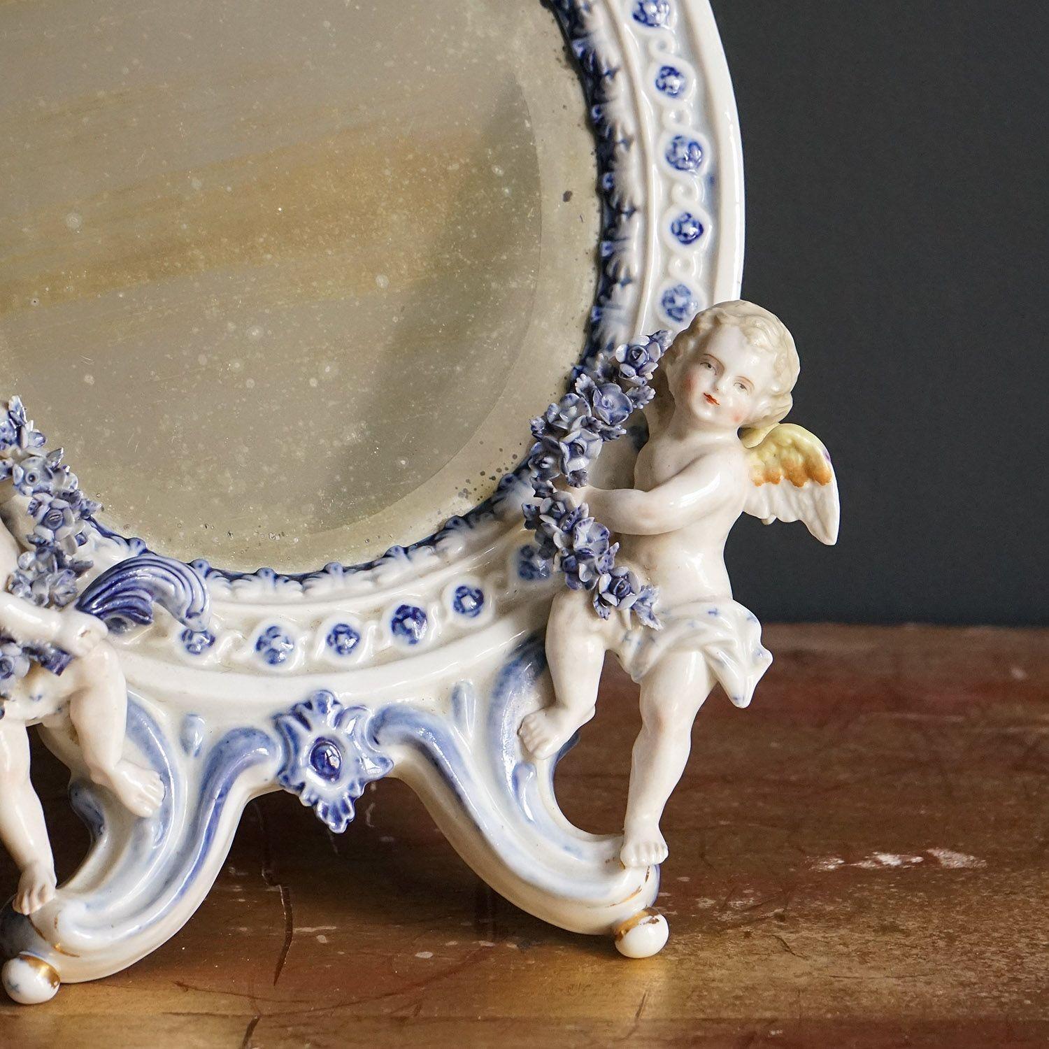 Miroir de toilette ovale en céramique

Un miroir en porcelaine de style rococo incrusté de guirlandes, de nœuds et de fleurs, flanqué de deux chérubins.

Plaque de miroir biseautée d'origine et dos de chevalet en bois.

Circa 1880 en date.

Il est