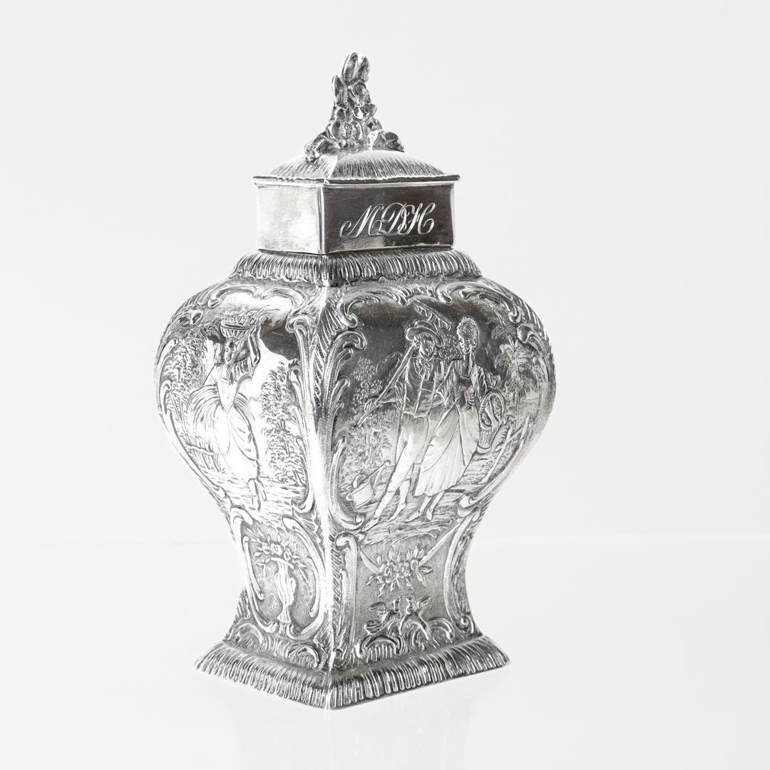 A fine antique German silver tea caddy.

In .800 silver.

By Georg Roth & Co.

Decorated throughout with repousse bucolic scenes and floral swags. The long edges both depict a man with a gardening rake arm in arm with a woman carrying a basket of