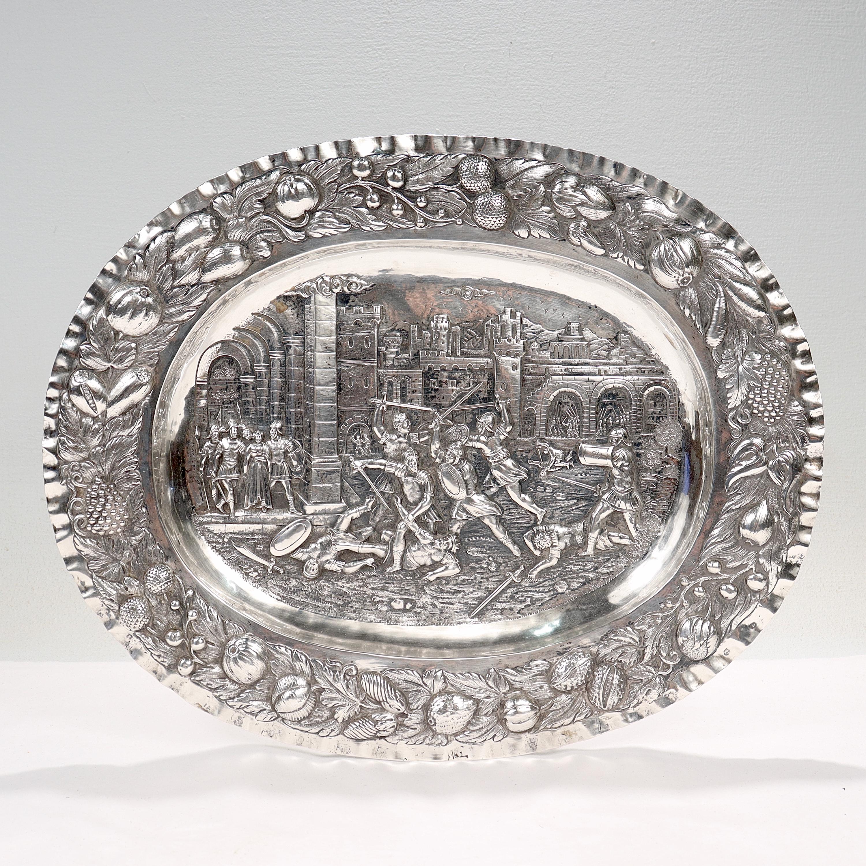 A fine antique Renaissance Revival German silver tray or charger.

In .800 silver.

Decorated with a repoussé battle scene. Soldiers are depicted battling one another within the walls of a Renaissance era city, with two regal looking women being