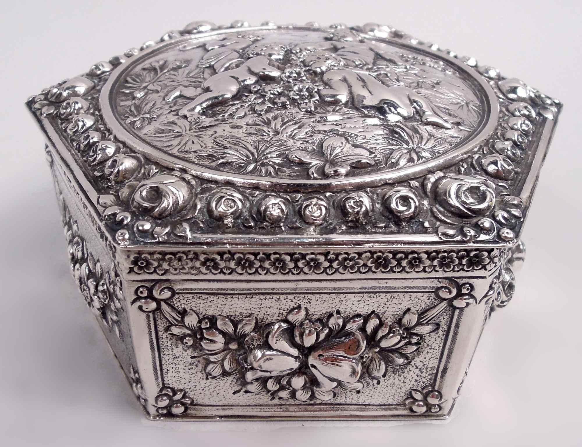 Boîte en argent rococo 800 allemande, vers 1900. Hexagonale à côtés droits ; guirlandes sur fond pointillé dans des cadres rectangulaires, et bordure en forme de tête de fleur. Couvercle légèrement soulevé ; grand rondel avec des chérubins ébauchés