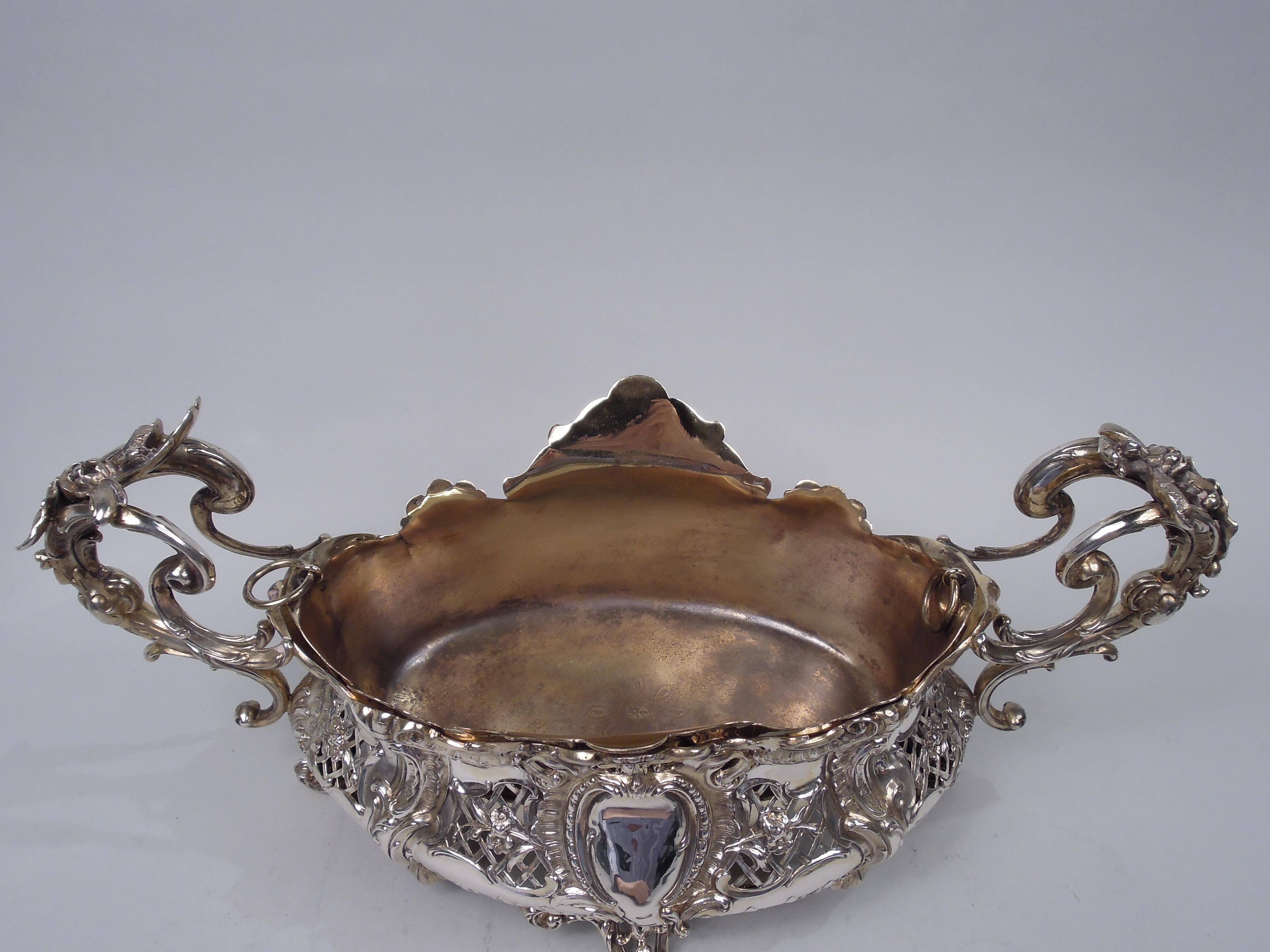 German Rococo 800 silver centerpiece, ca 1900. Ovoid and bellied bowl with leaf and flower-capped split-mounted double-scroll end handles, and four scroll-mounted supports. Exuberant leafing scrolls, layered scallop shells, and open flower-strewn