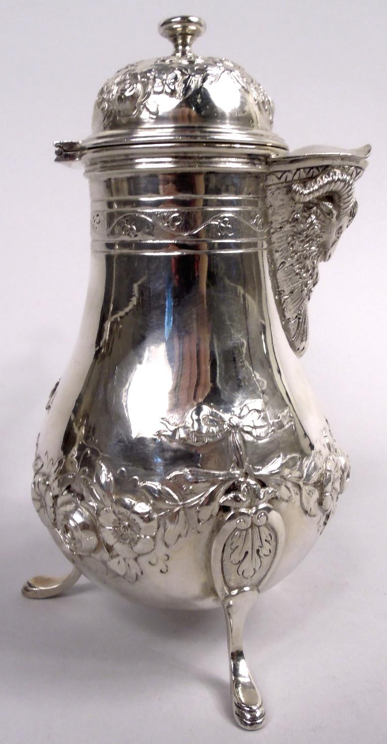 Cafetera rococó alemana de plata 800, hacia 1900. Cuenco con balaustres y soportes para cascos montados en volutas. Caño en V, tapa abatible y abovedada, y asa torneada de madera teñida. Guirnaldas de cintas evocadoras de retozos galantes.