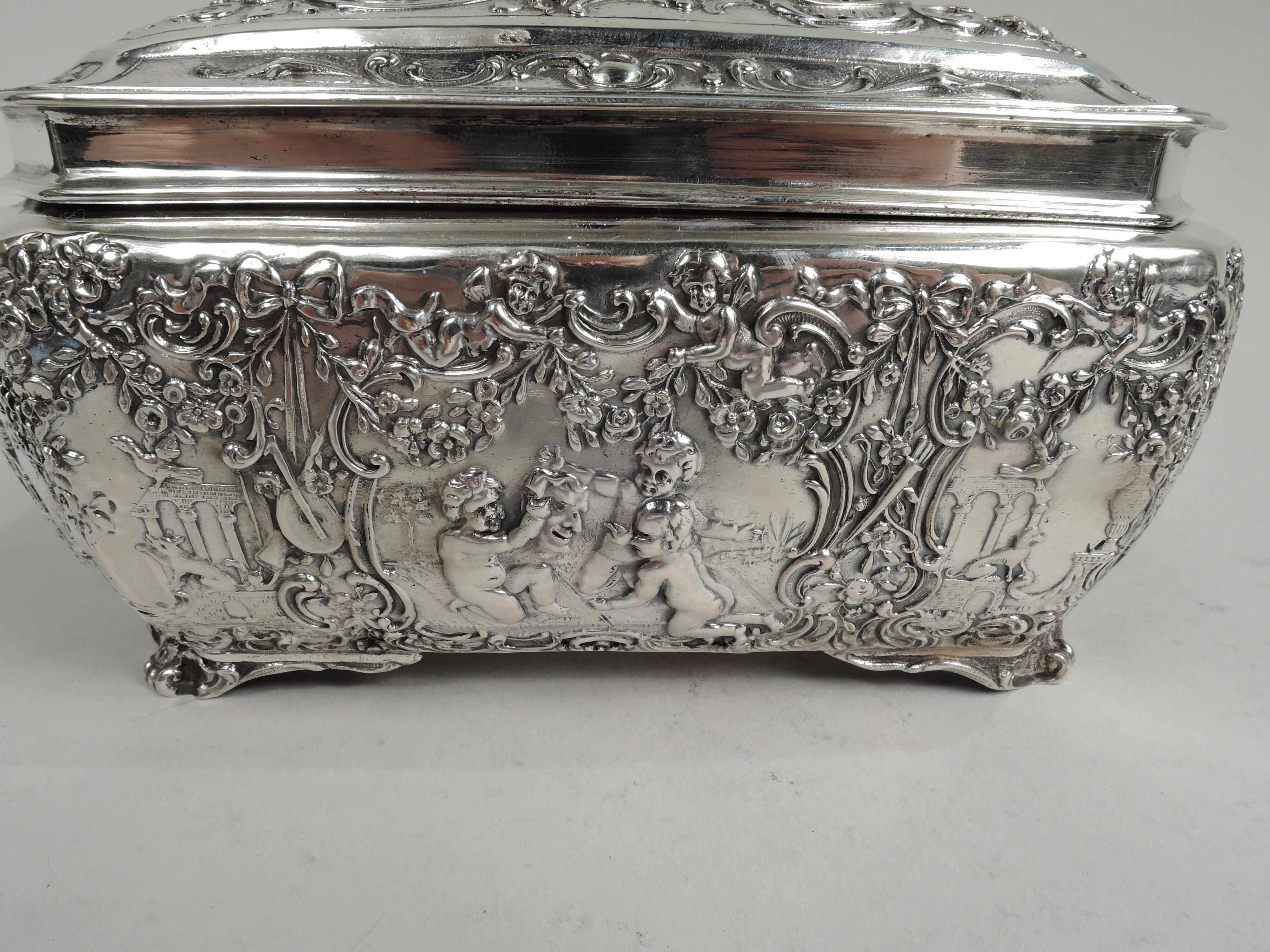 Turn-of-the-century German Rococo 800 silver box. Rectilinear with tapering sides and chamfered corners with scroll supports. Cover hinged, raised, and inset. Chased ornament with chubby, bare bottomed cherubs with adroitly arranged drapery