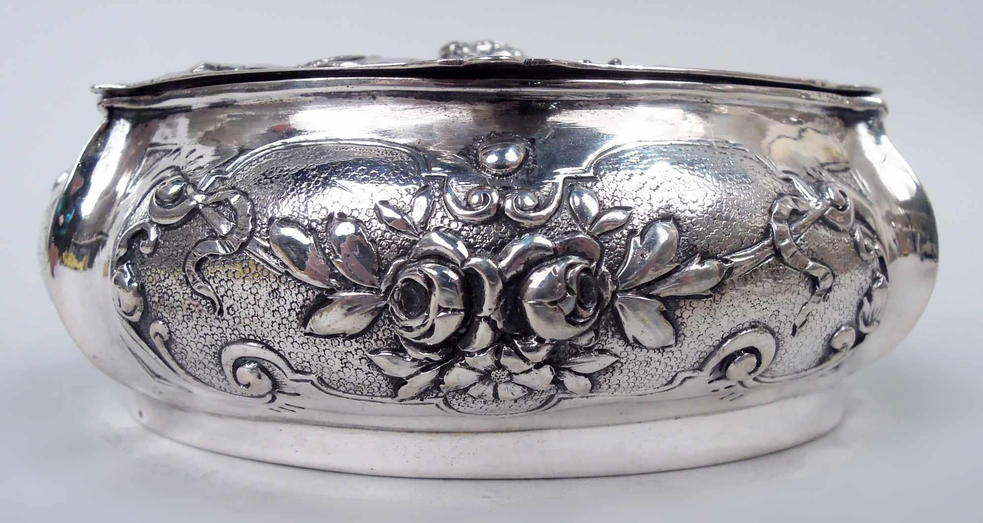 Boîte à bibelots en argent de style rococo allemand avec des chérubins, vers 1900. Ovale ; lobé et ventru. Sur les côtés, des cadres à volutes avec des guirlandes sur fond pointillé. Couvercle à charnière et à onglet ; sur le dessus, en haut relief,