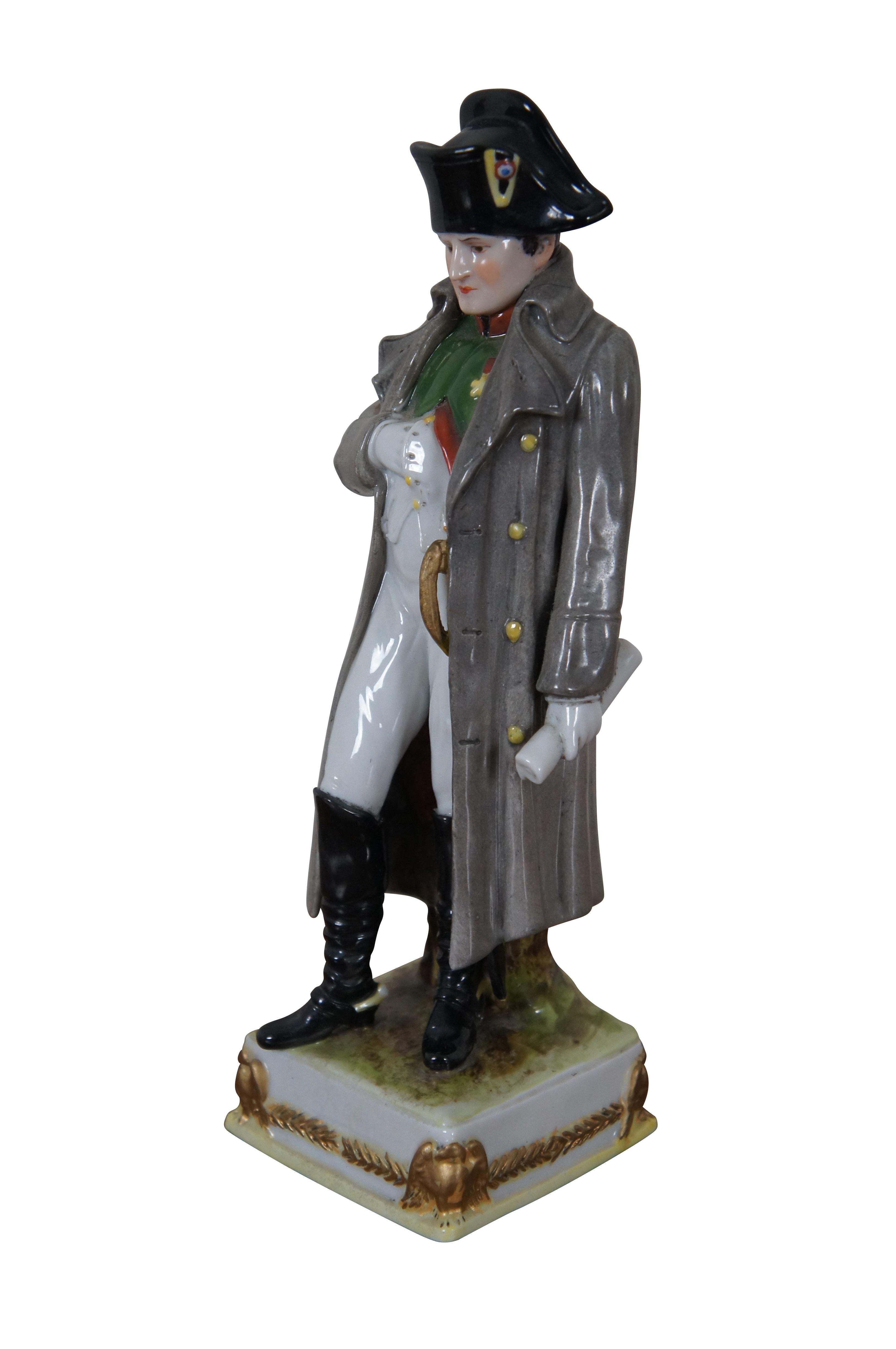Antique German Scheibe-Alsbach / Sitzendorf / Kister porcelain figurine of General Napoleon Bonaparte wearing traditional attire with long overcoat, holding a scroll, standing on a gold eagle lined base.

Dimensions:
2.75” x 2.75” x 9” (Width x