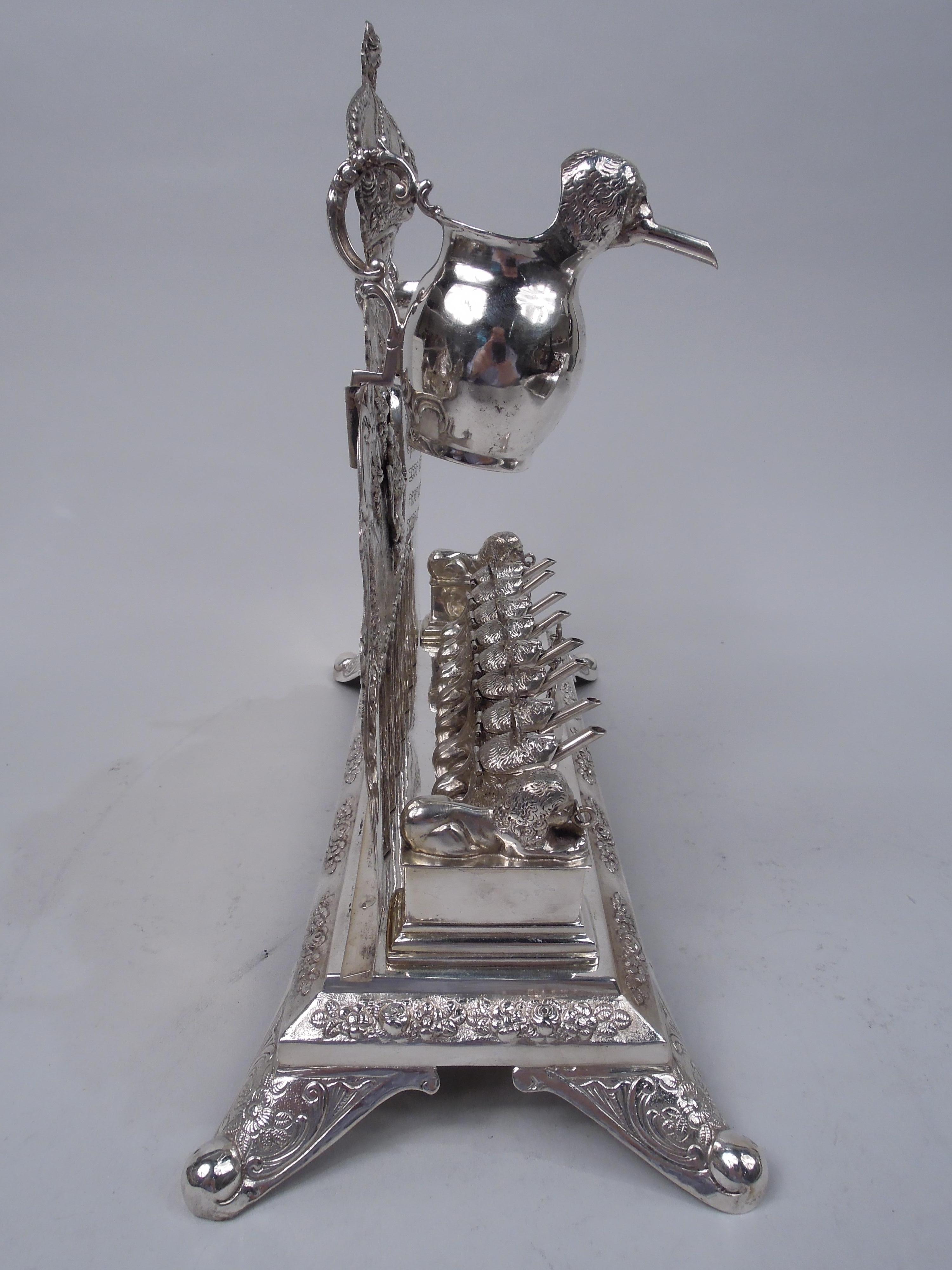 German 800 silver menorah, ca 1900. Scrolled back with crown, chased interlaced scrolls, and half fluting; applied Torah between lions rampant and two detachable lion-head oil pitchers mounted to top. Rectangular base on 4 splayed corner supports.