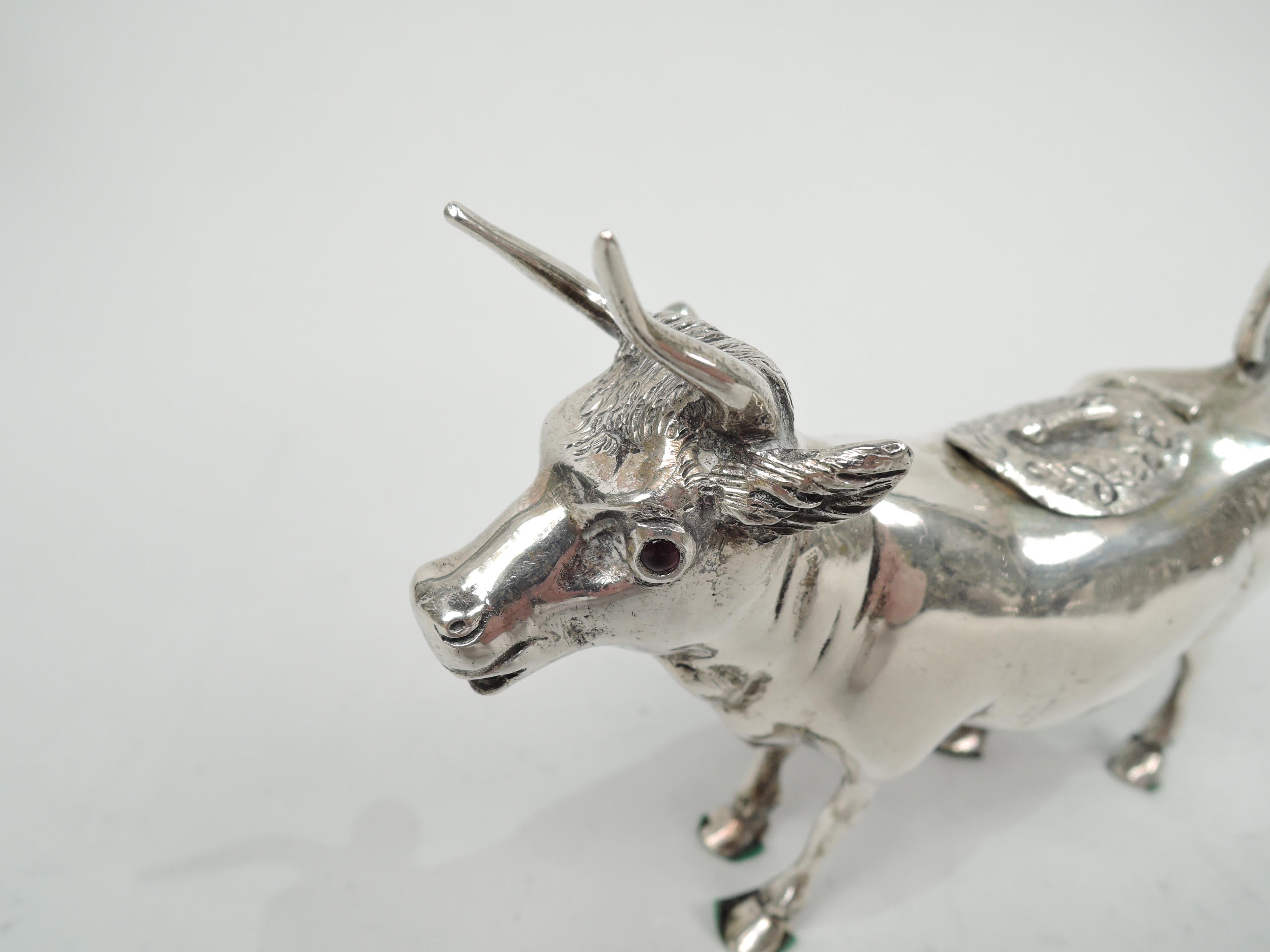 German 800 silver cow creamer, circa 1910. A sweet and alert face with red glass eyes, flexed ears, and big pointy horns. Sturdy body with hinged and tooled back cover and ring tail handle. Slender legs and firmly planted hoofs. A nice breakfast