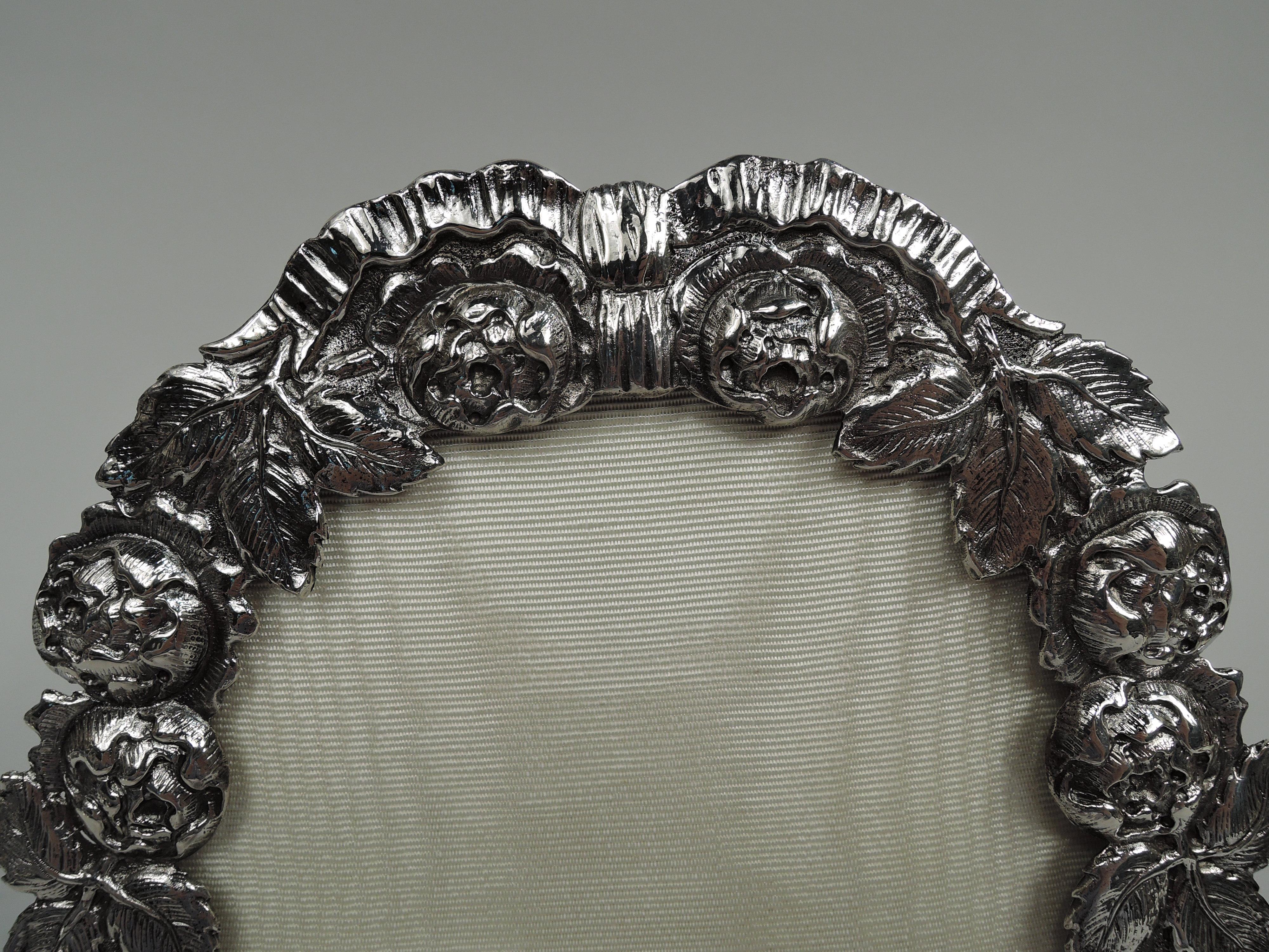 German 800 silver picture frame, circa 1920. Oval window in chased and tooled surround comprising flower heads and leaves. Textural with irregular rims. With glass, silk lining, and velvet back with hinged easel support. With loose-mounted ring. For