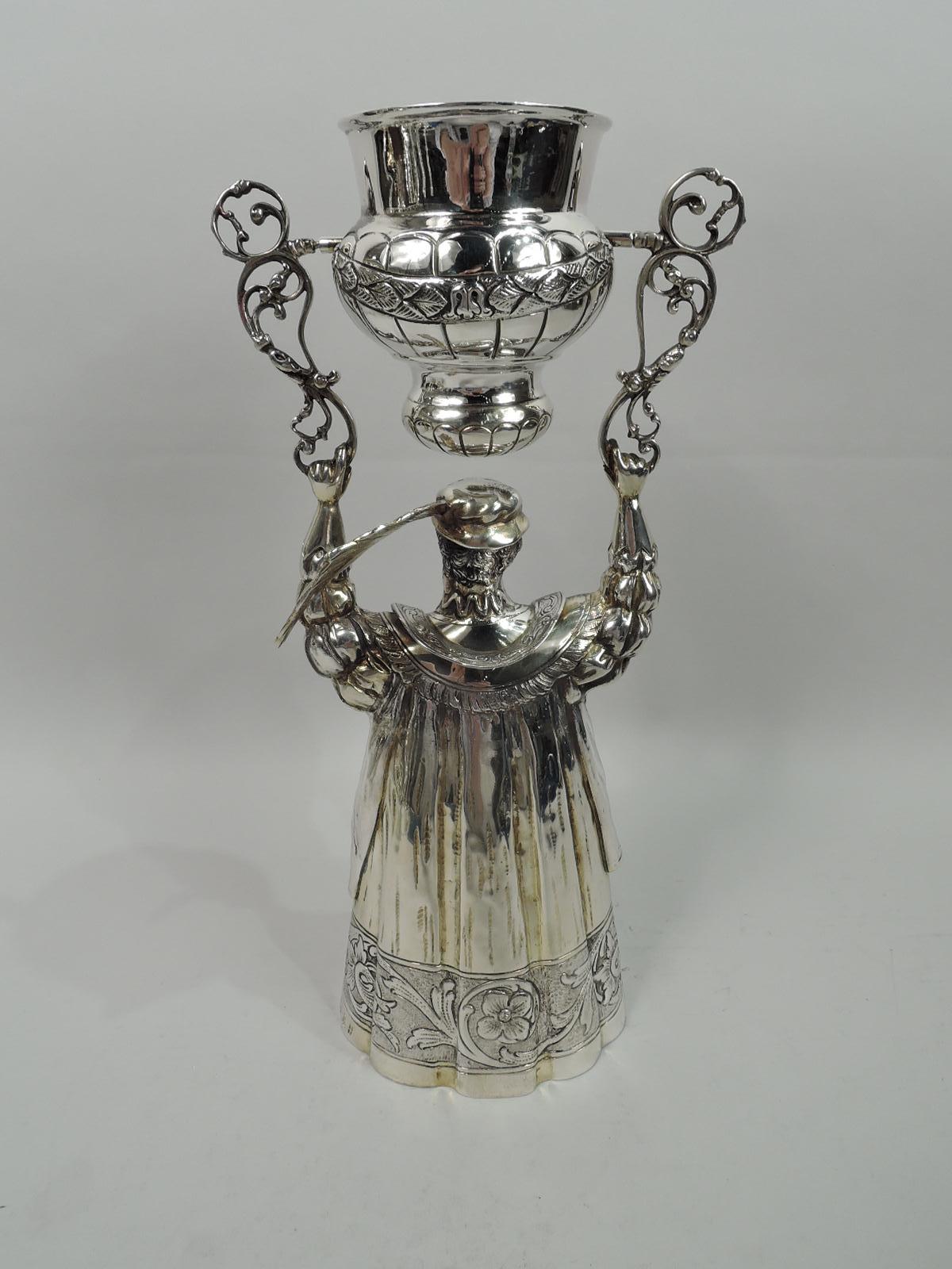 German parcel gilt sterling silver male figural wedding cup, ca 1920. A 16th-century grandee with feathered cap holds aloft a bellied cup swing-mounted to scroll brackets. His robe with neat folds and flowering scroll border forms the second cup.