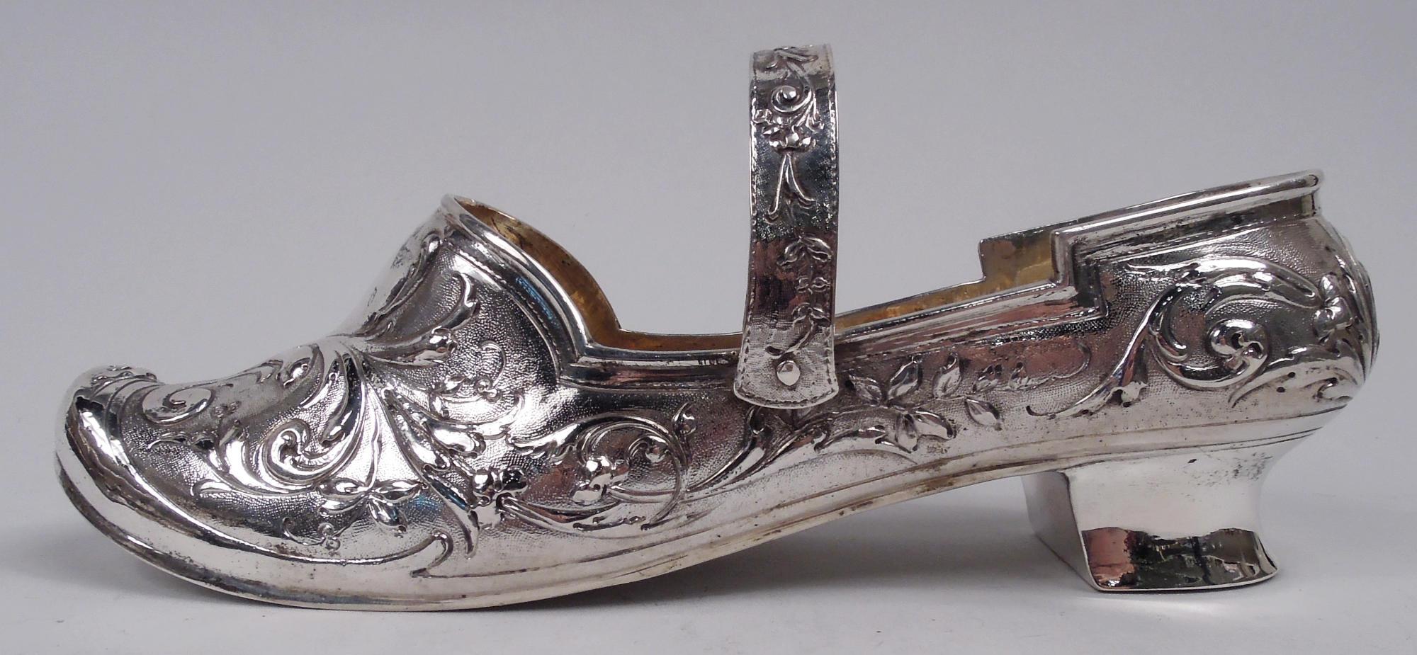 German 800 silver lady’s shoe, ca 1920. Plain sole and low heel, and loose-mounted c-scroll strap. Chased leafing and flowering scrolls on stippled ground. Hanau marks. Heavy weight: 6.8 troy ounces. 