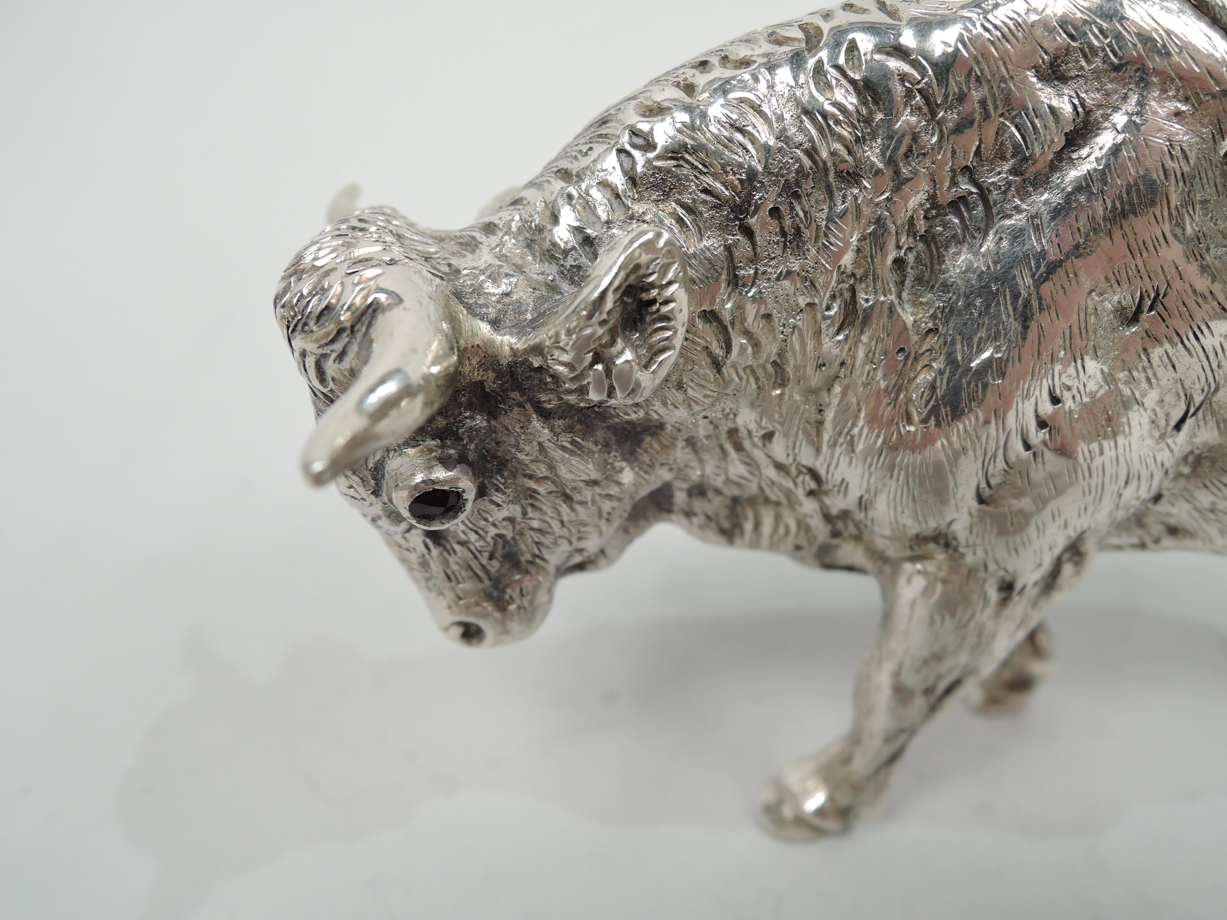 German 800 silver cast bull creamer. Shaggy boy beast with drooping tail, ambling along muscular legs. Head downturned with flicked-back ears, sharp horns, mouth spout, and red glass eyes. Hinged back-flap with fly finial. Marks include stamp for