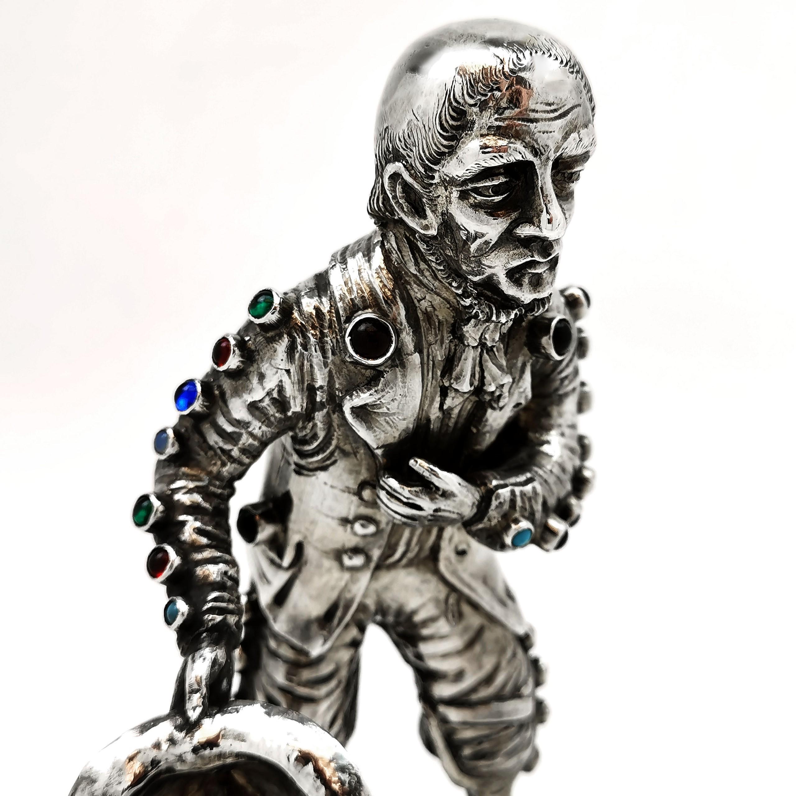 A lovely antique German solid silver model figure of a man inset with coloured cabochon stones. The man appears to be begging, holding out his hat with a poignant expression on his face. He has a wooden peg leg and stands on a stone set