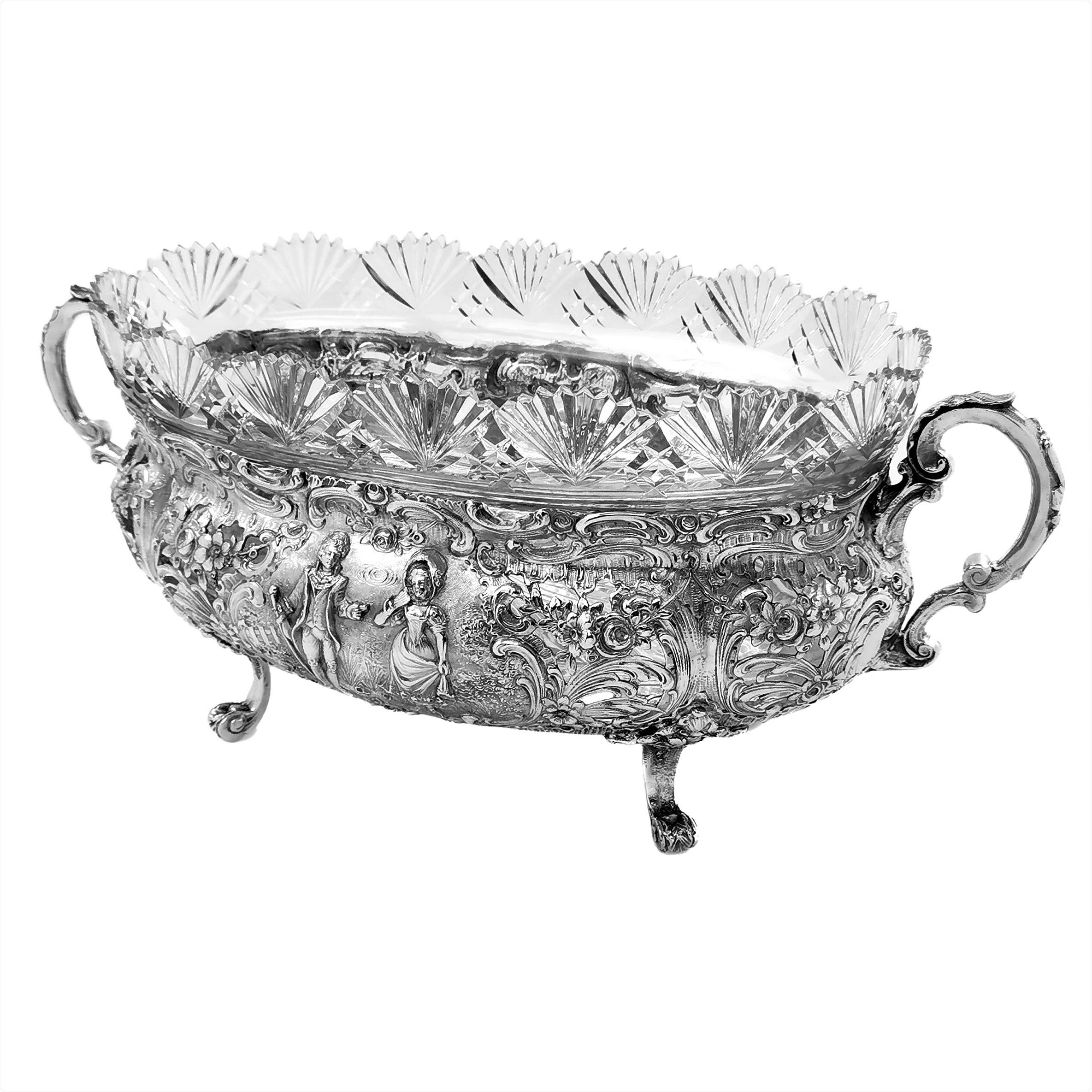 A magnificent antique German solid Silver Bowl with a ornate chased design on the body and two scroll handles. The chased designs show detailed classical scenes surrounded by elaborate floral and scroll designs. The Bowl has a fitted clear glass