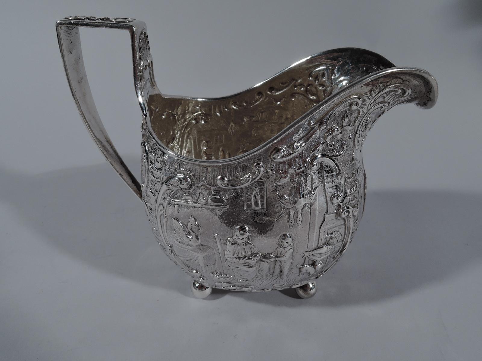 Pair of German sterling silver creamer and sugar, circa 1920. Curved bodies, corner ball supports, and high-looping scroll bracket handle. Creamer has u-form lip spout. Chased olden-days scenes with country folk at home with blazing hearth and