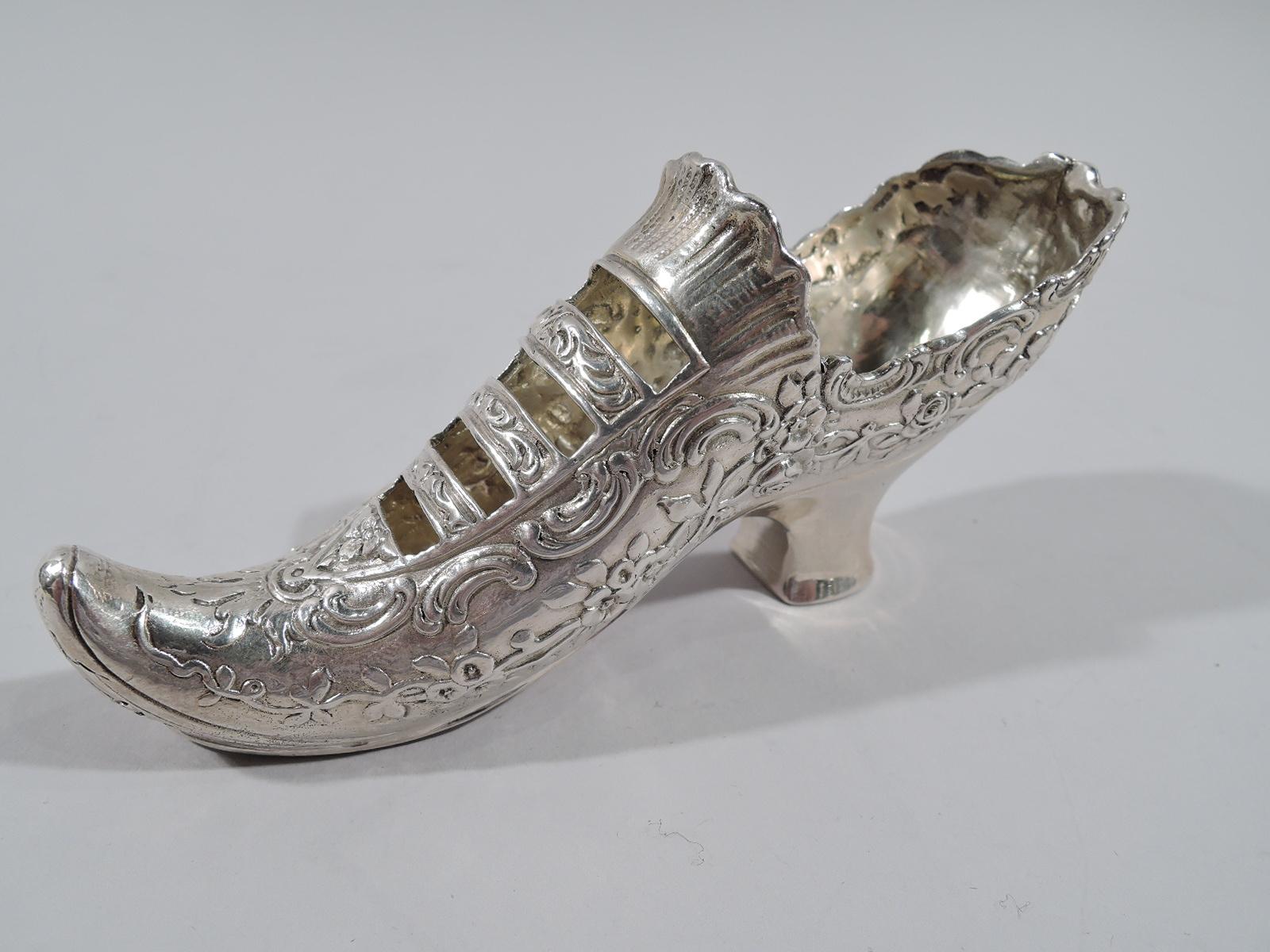 German sterling silver miniature elf shoe. Imported to England in 1904 by Berthold Muller in Chester. Rococo shoe with chased scrolls and flowers. Open bands and raised elf toe. Heel plain. German maker’s and English importer’s marks. Weight: 2.7