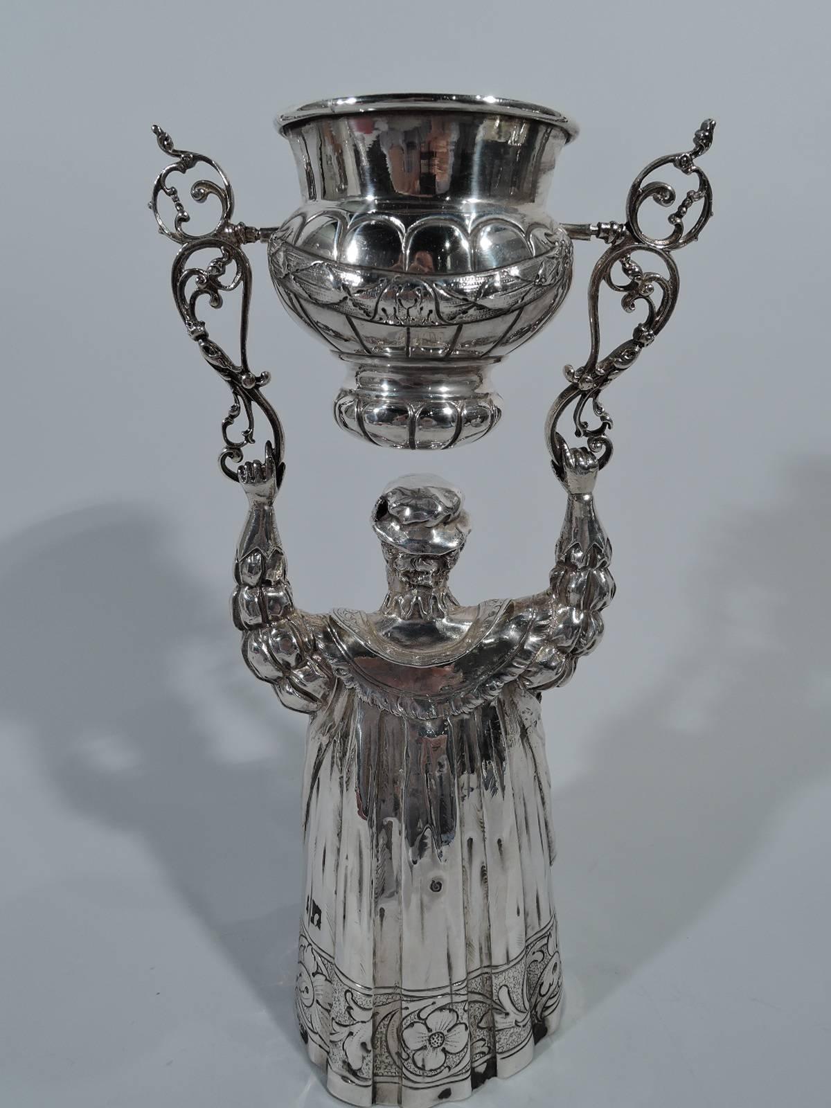 German sterling silver wedding king cup. Imported to Chester, England by Berthold Muller in 1901. A Renaissance prince holds aloft scrolled brackets to which are swing-mounted a lobed and double-domed cup. Period costume in form of sumptuous robe