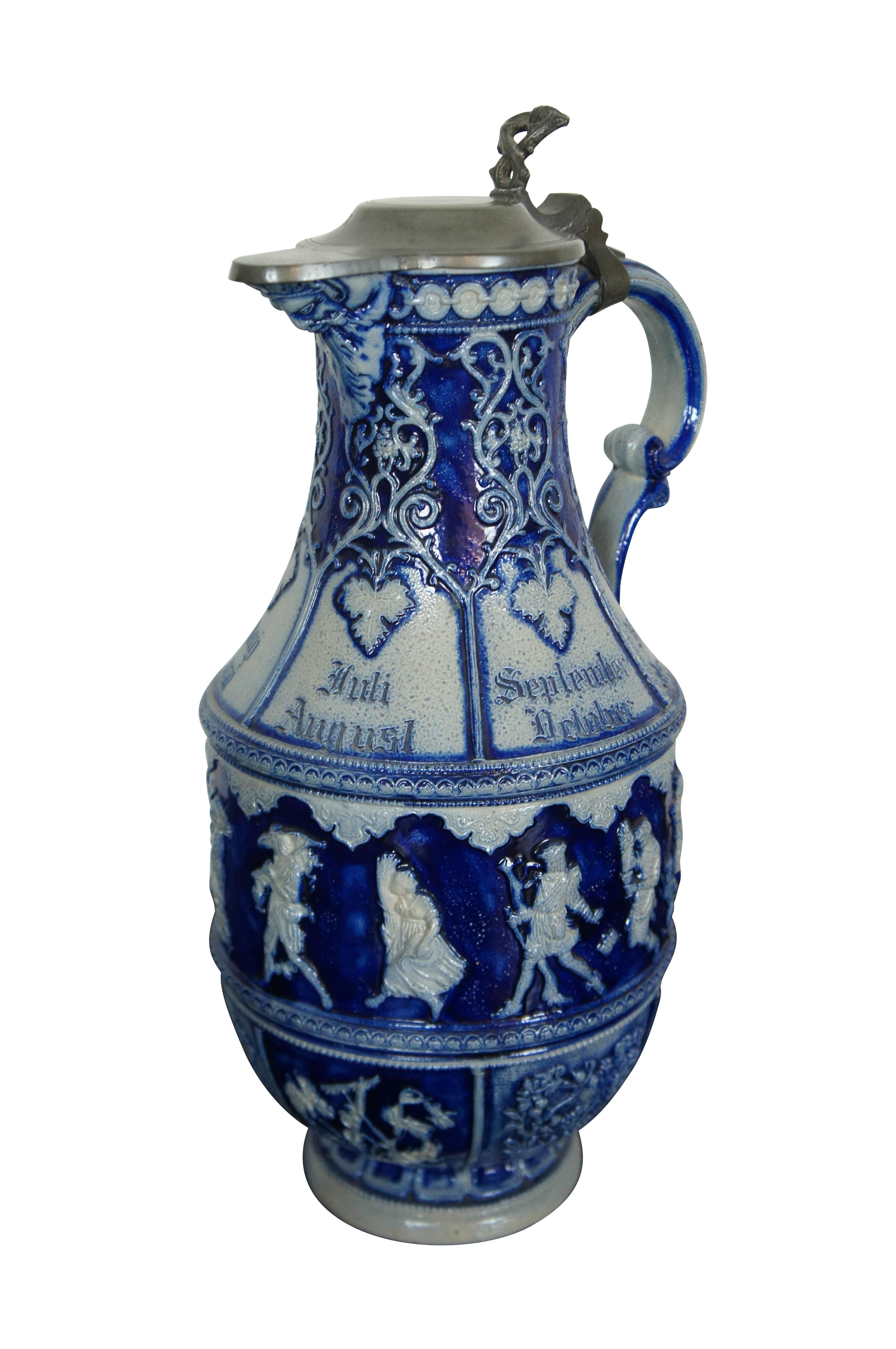 Antique German cobalt blue salt glaze pewter lidded stoneware pitcher / jug / ewer featuring the face of Dionysus or Bacchus - God of wine - on the spout surrounded by grapevines / grapes / leaves, the months of the year and dancing