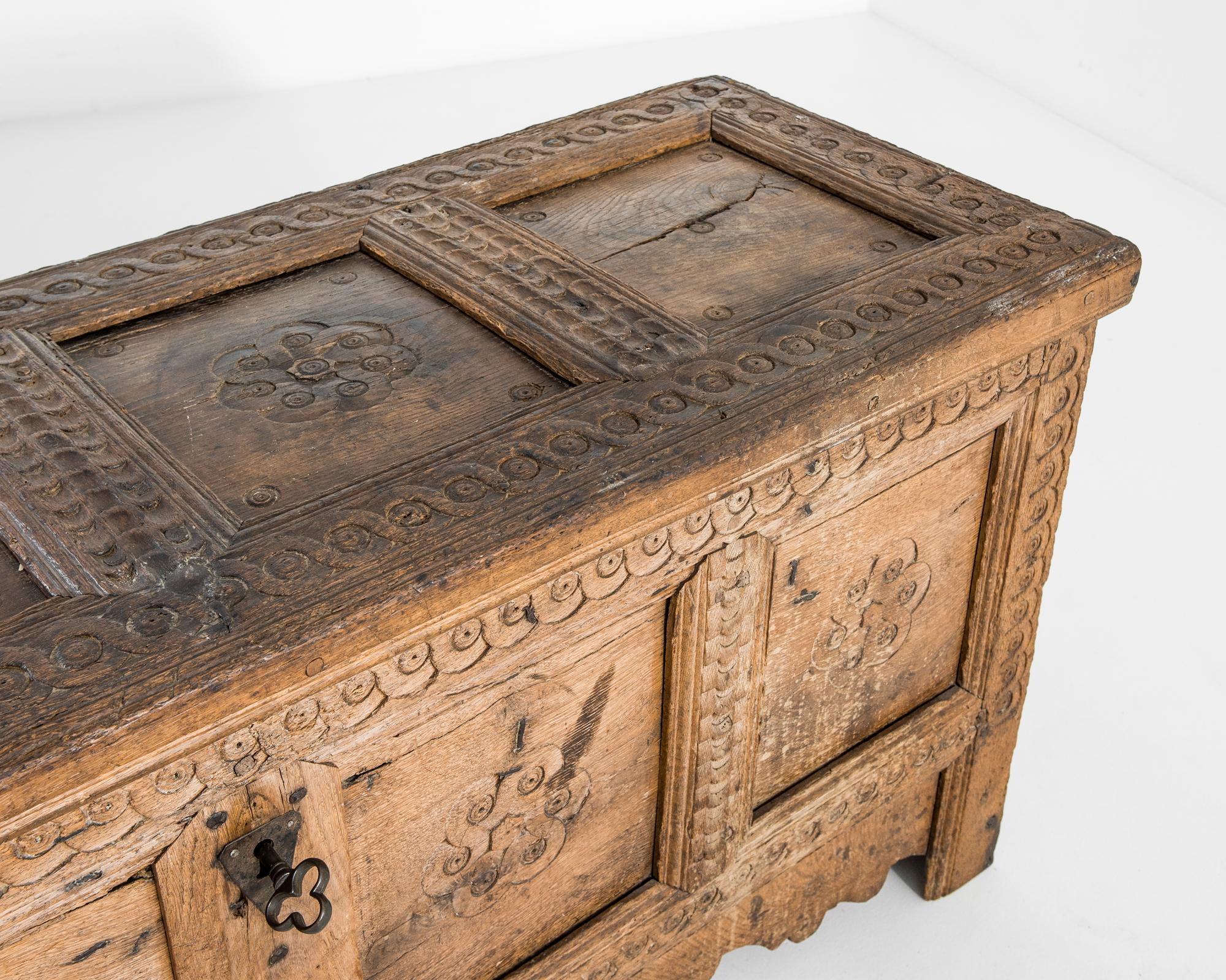 A provincial wooden trunk from 1800s Germany. The charming case is decorated with carved spiral patterns intertwined in a floral embrace. The chest is elevated, its feet complemented with an original scalloped apron that subtly contrasts with the