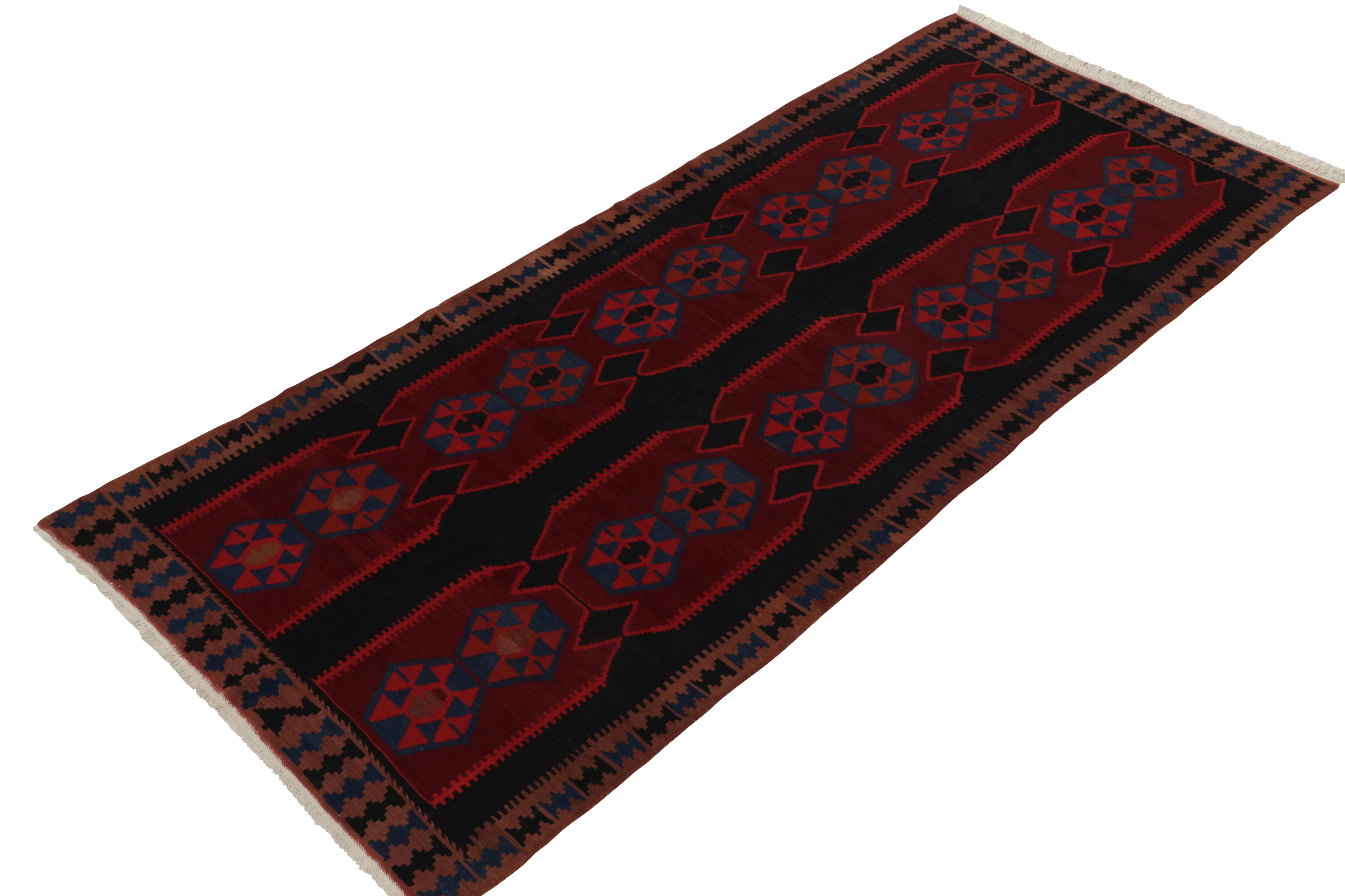 Handwoven in wool from Persia circa 1950-1960, a vintage Ghazvin kilim rug boasting an atypical design. The vision carries geometric repetition in deep reds, browns & blues with natural movement on a rare black background. Exemplifying mid century